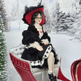Load image into Gallery viewer, “Winter Lady” Doll in a black and white outfit with a red hat sitting in a sleigh in a snowy landscape.
