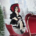 Load image into Gallery viewer, “Winter Lady” Doll in a winter scene with a red sleigh and snow-covered trees.
