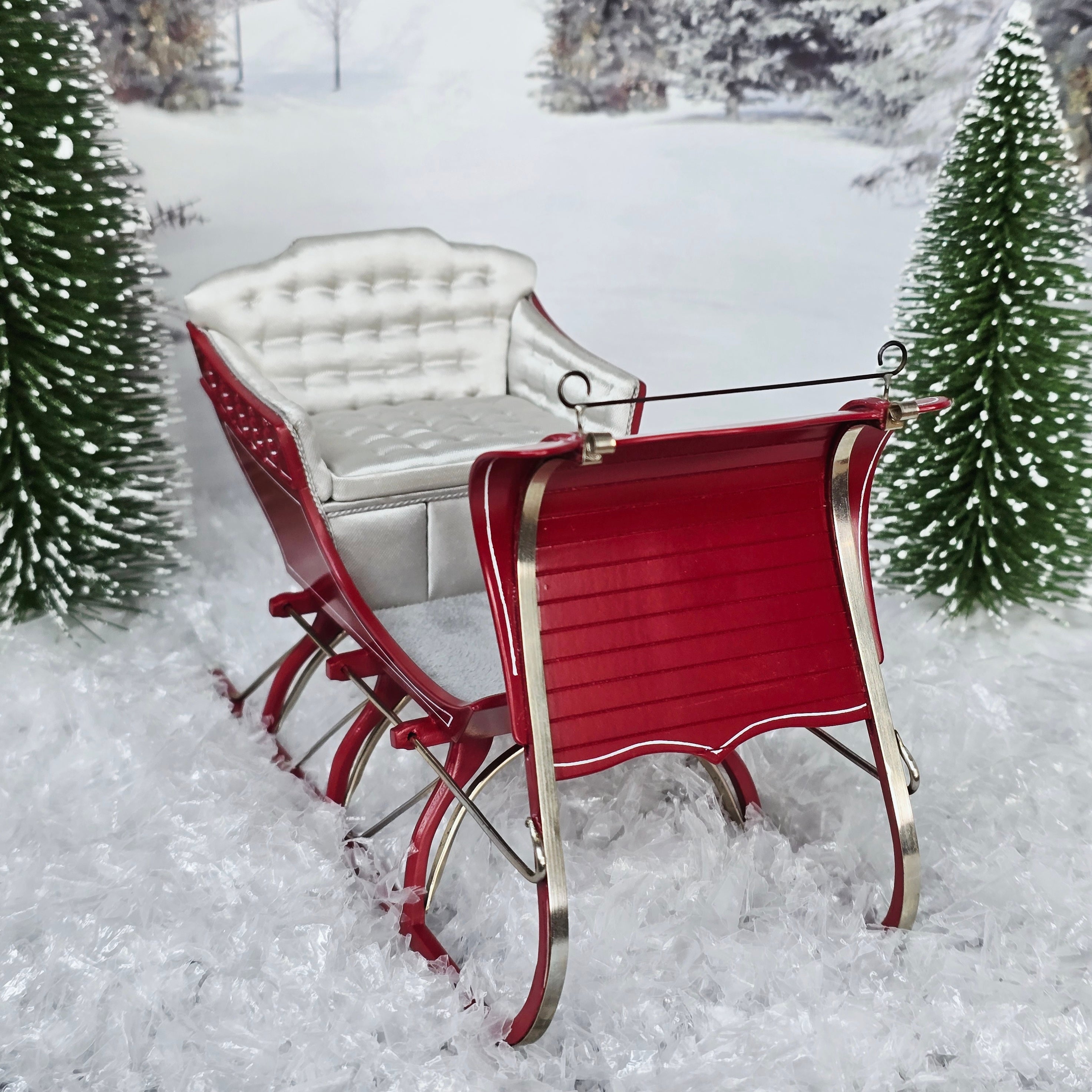 Red sleigh with white seat in a snowy landscape with Christmas trees.
