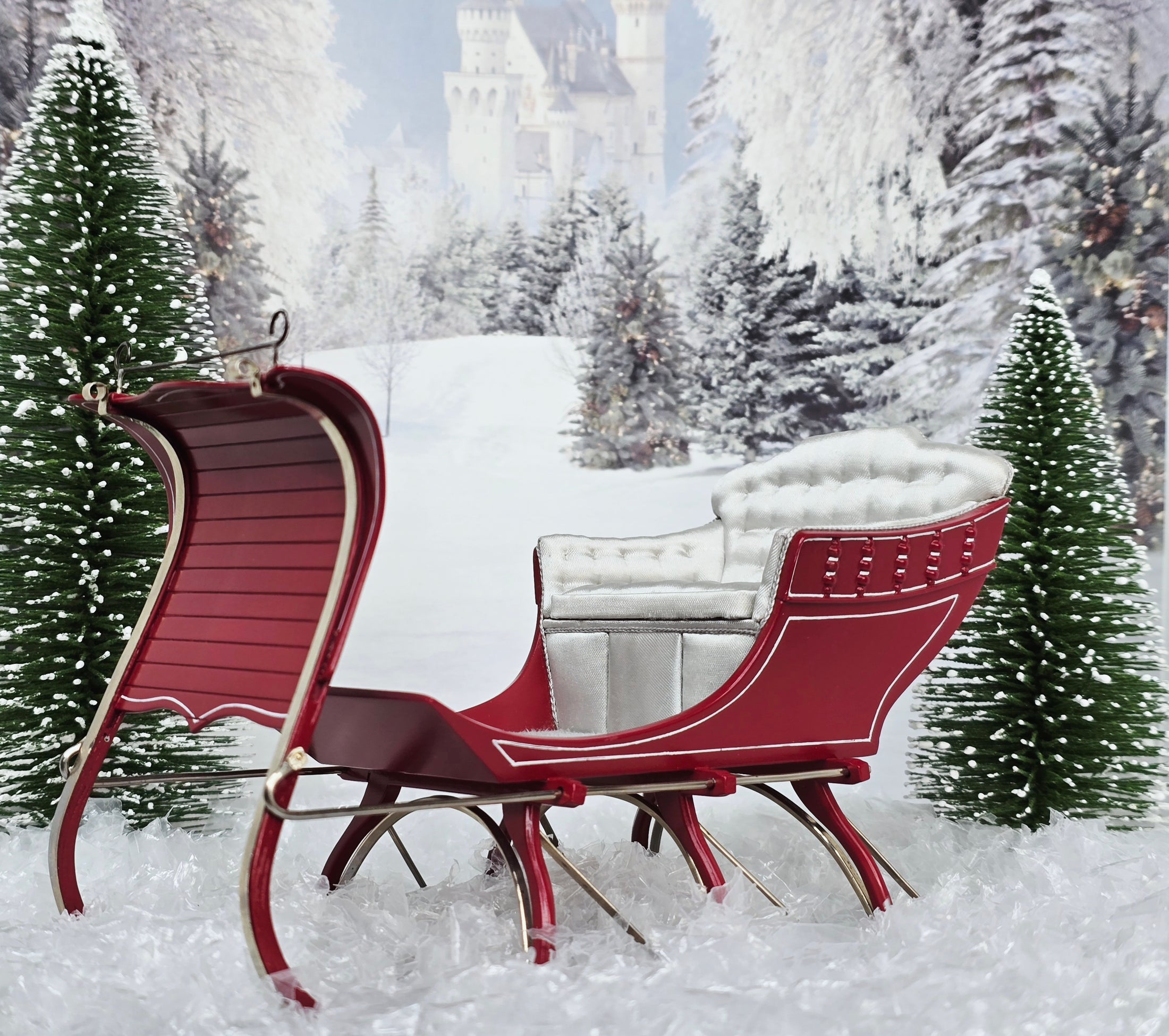 Red sleigh with white seat in a snowy landscape with trees and a castle.