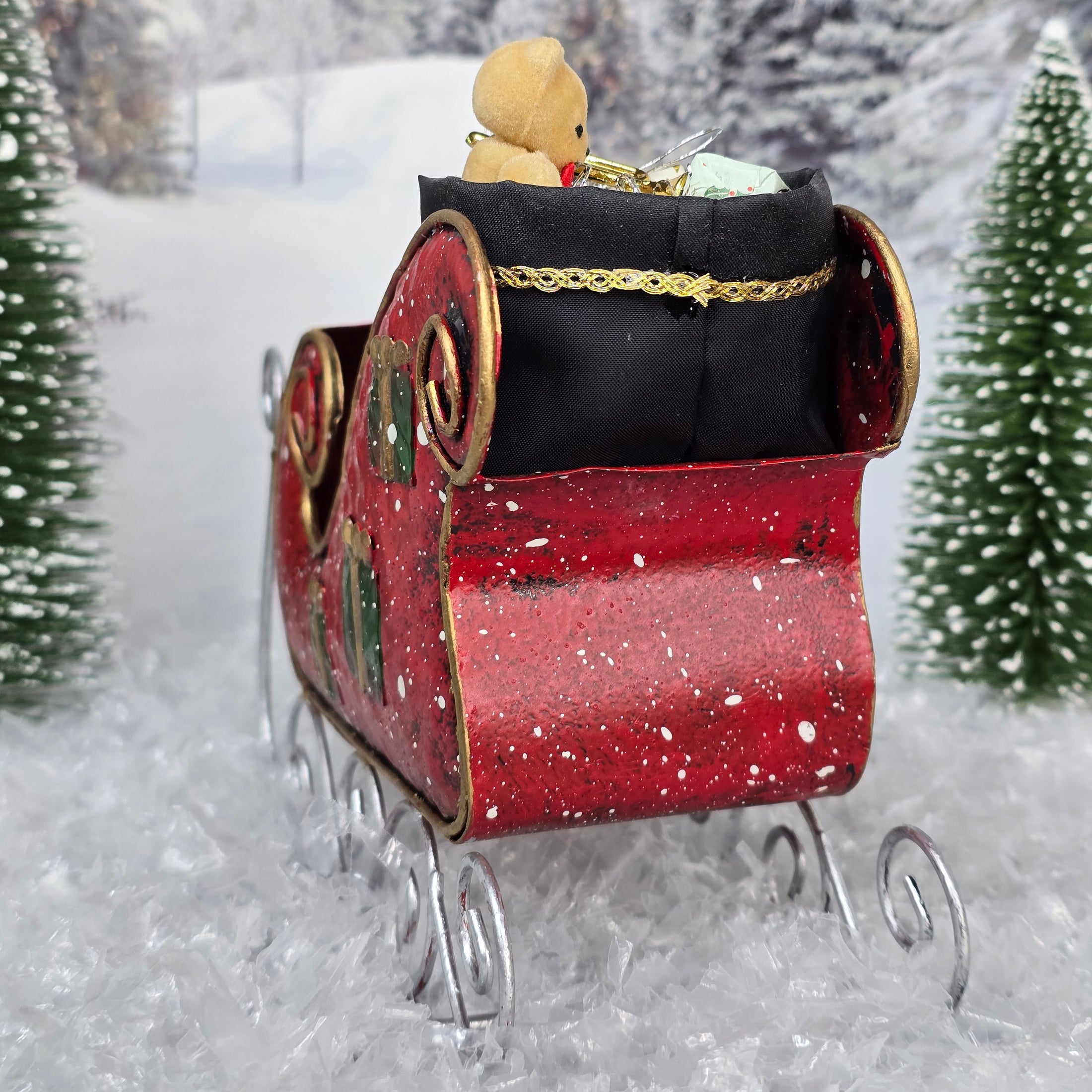 Red toy sleigh with a teddy bear in a snowy landscape, back view