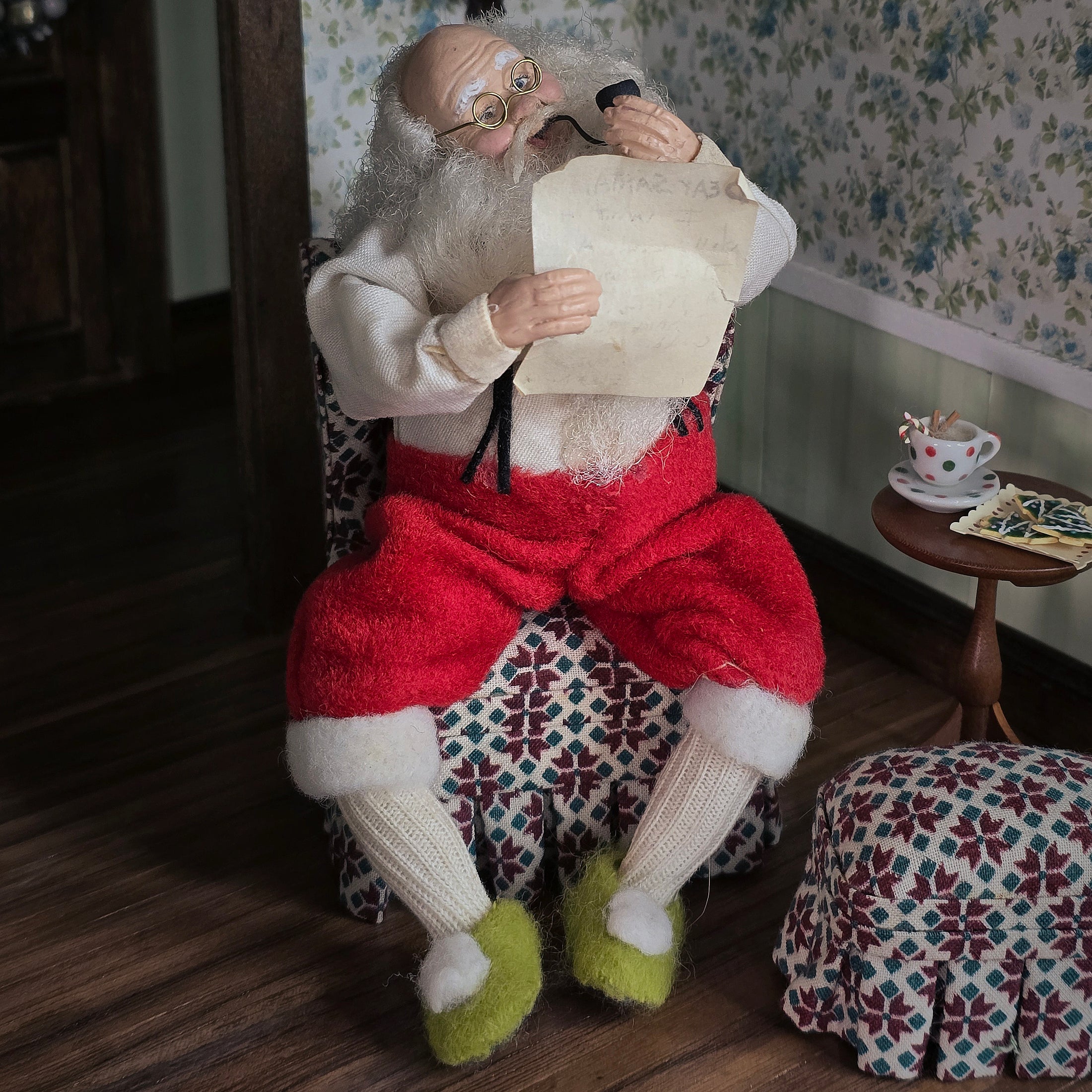 Santa Claus doll sitting in a chair with a patterned floral wallpaper background