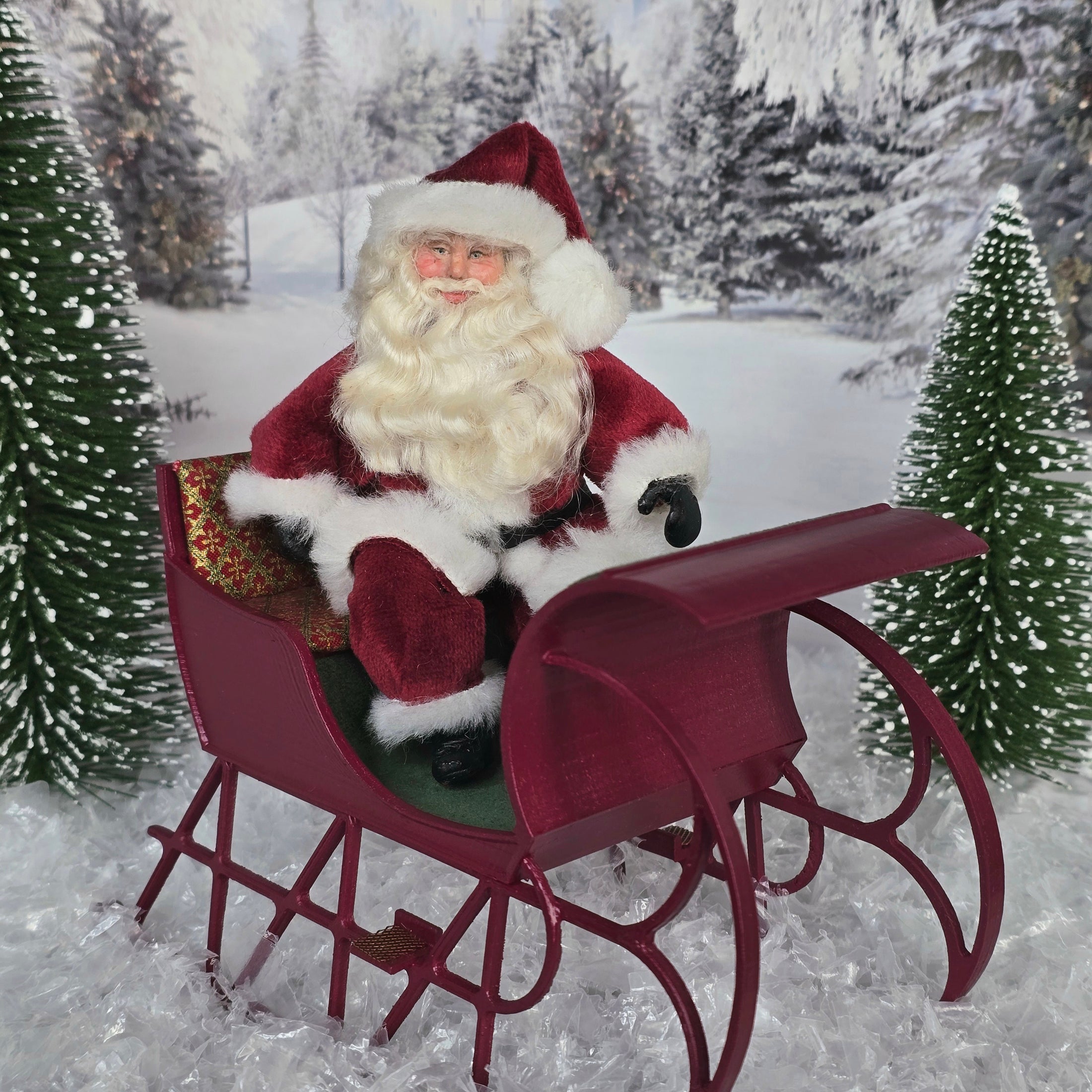 Santa Claus dollhouse doll sitting in a sleigh in a snowy landscape with trees.