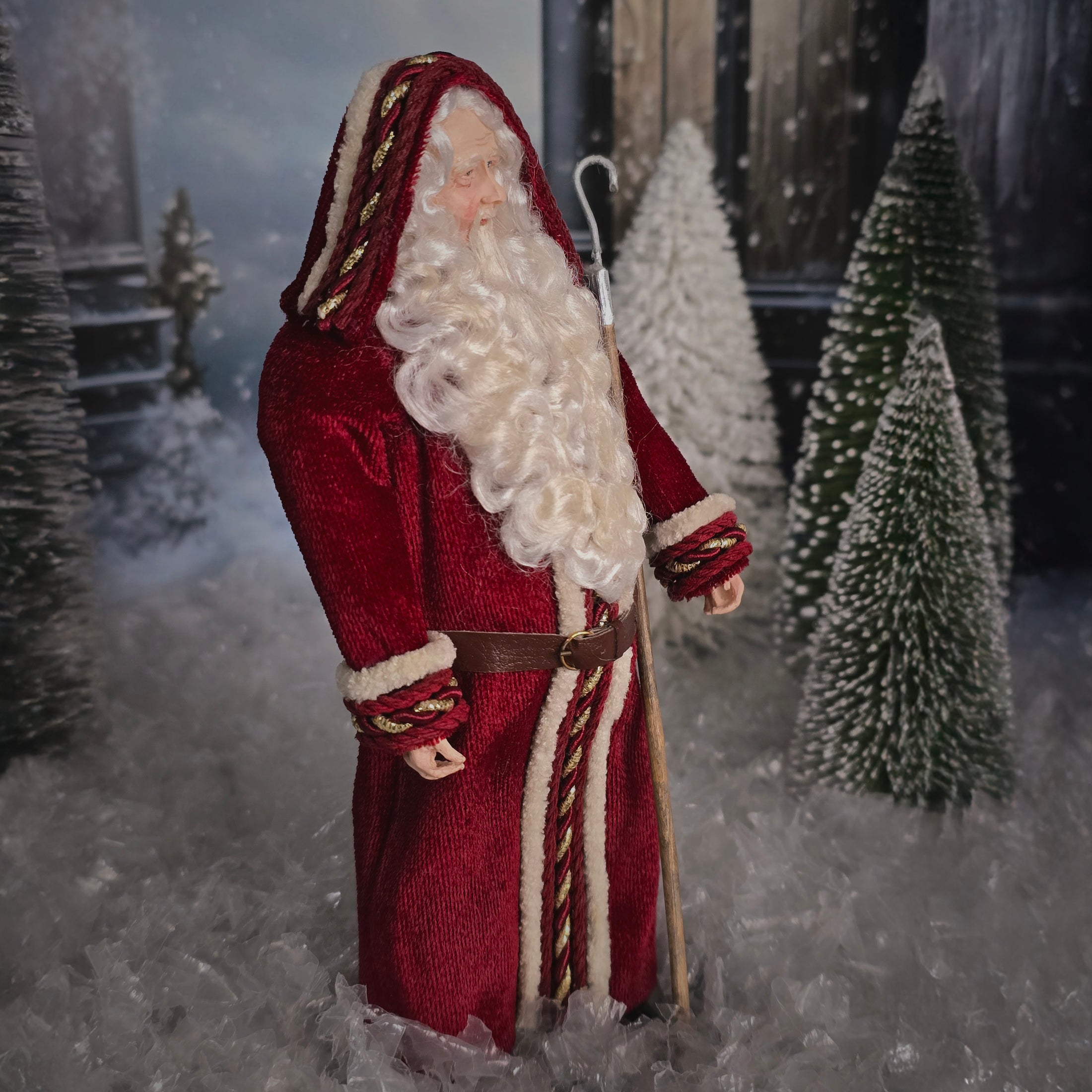 Santa Claus doll in a snowy scene with trees and a house.