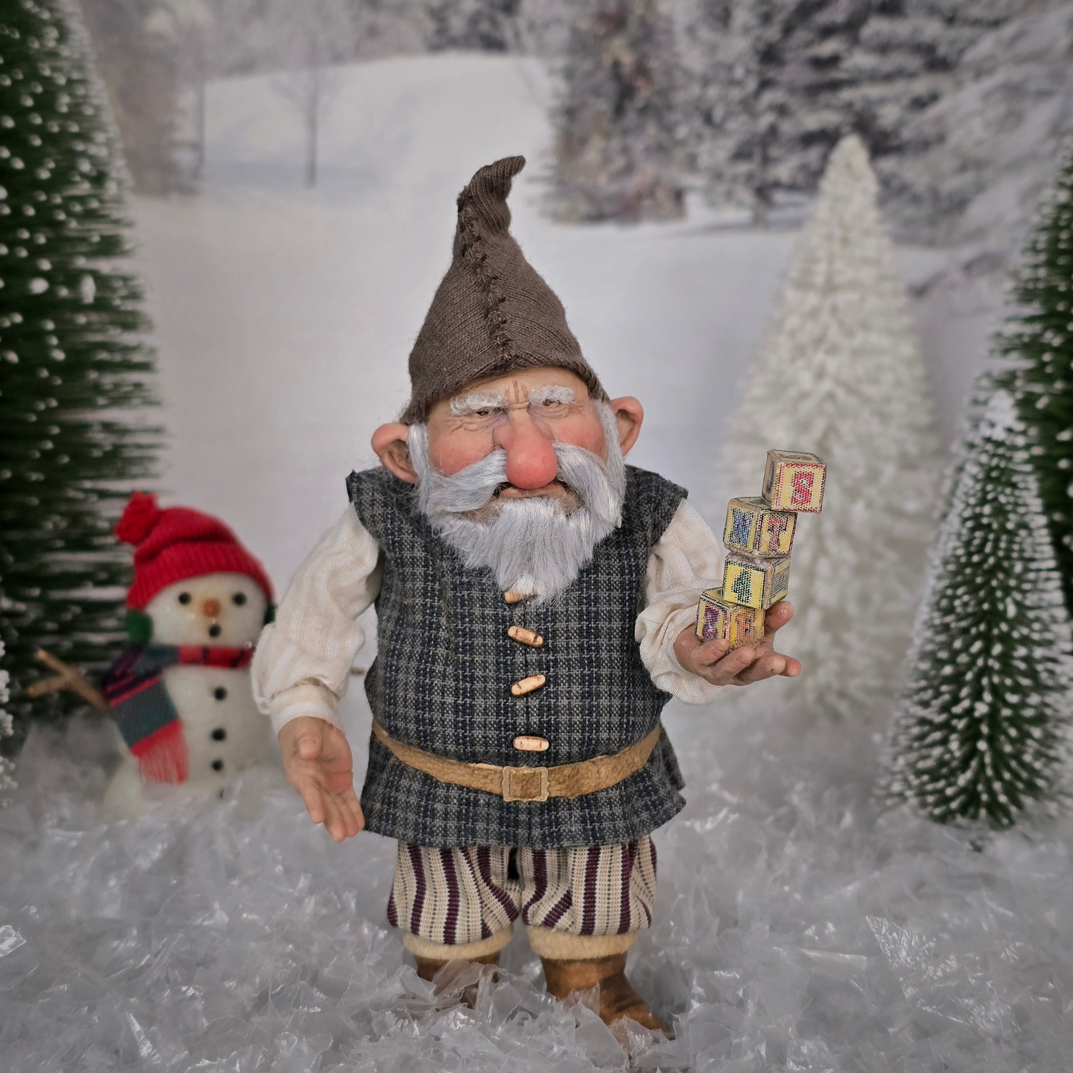 Sharon Cariola Elf dollhouse doll holding wooden blocks in a snowy landscape with a snowman and trees.