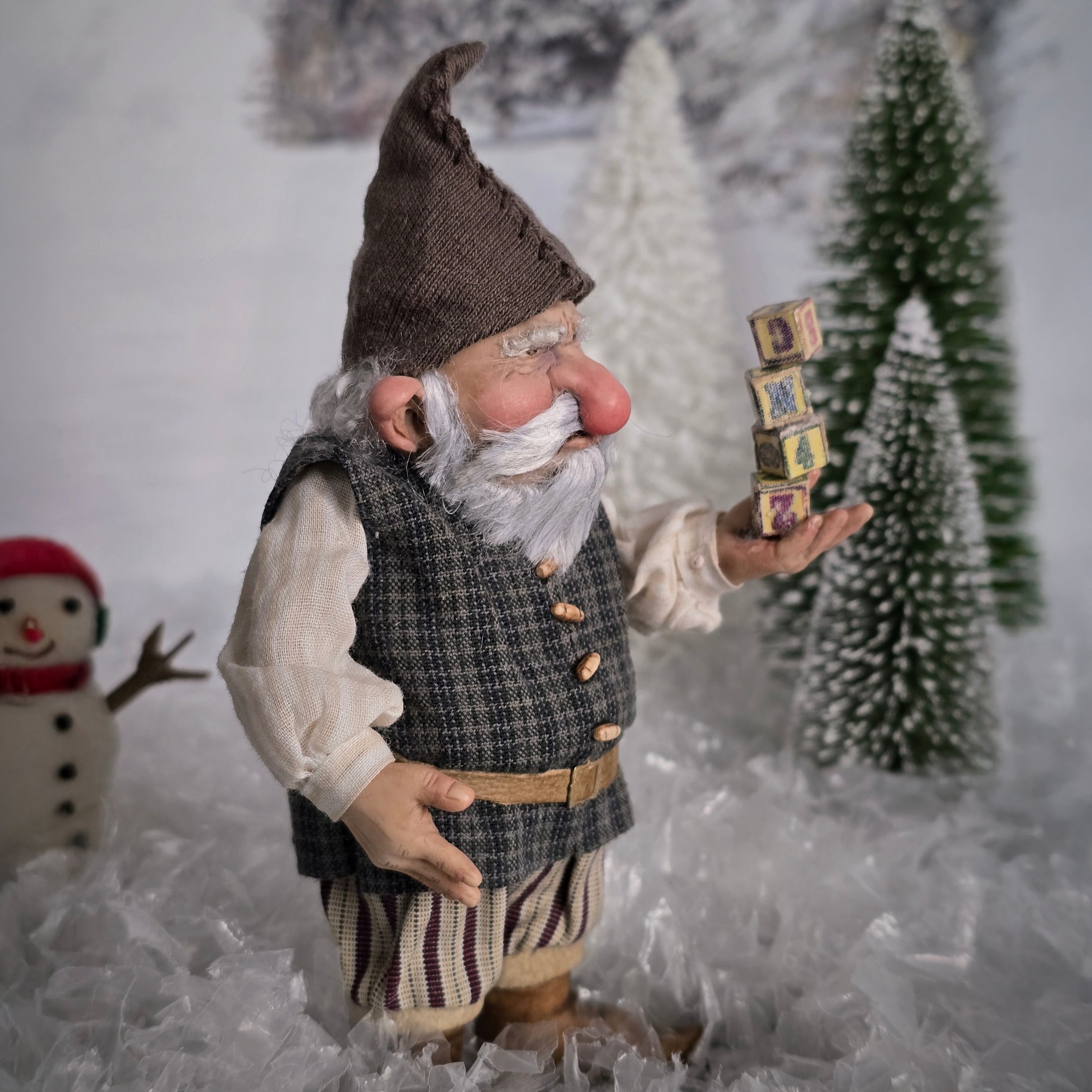 Sharon Cariola Elf dollhouse doll  holding small blocks in a snowy scene with trees and a snowman.