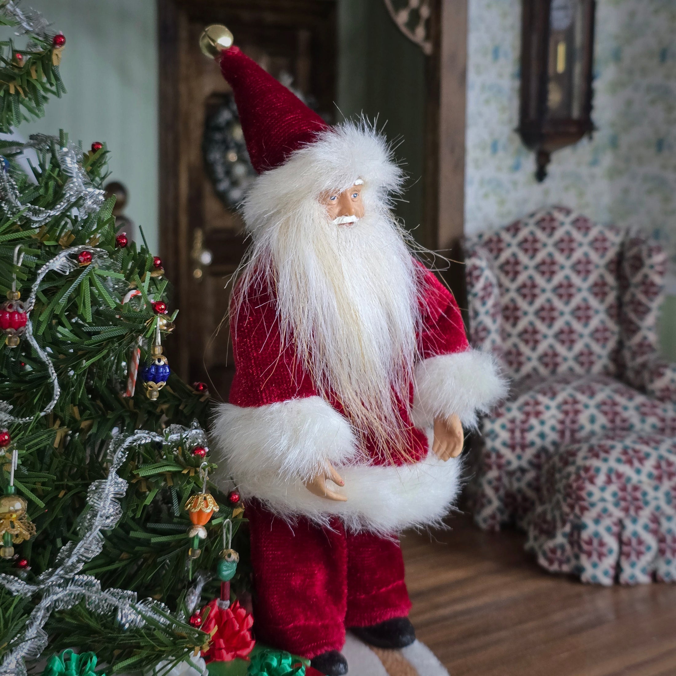 Santa Claus dollhouse doll next to a decorated Christmas tree in a festive room.