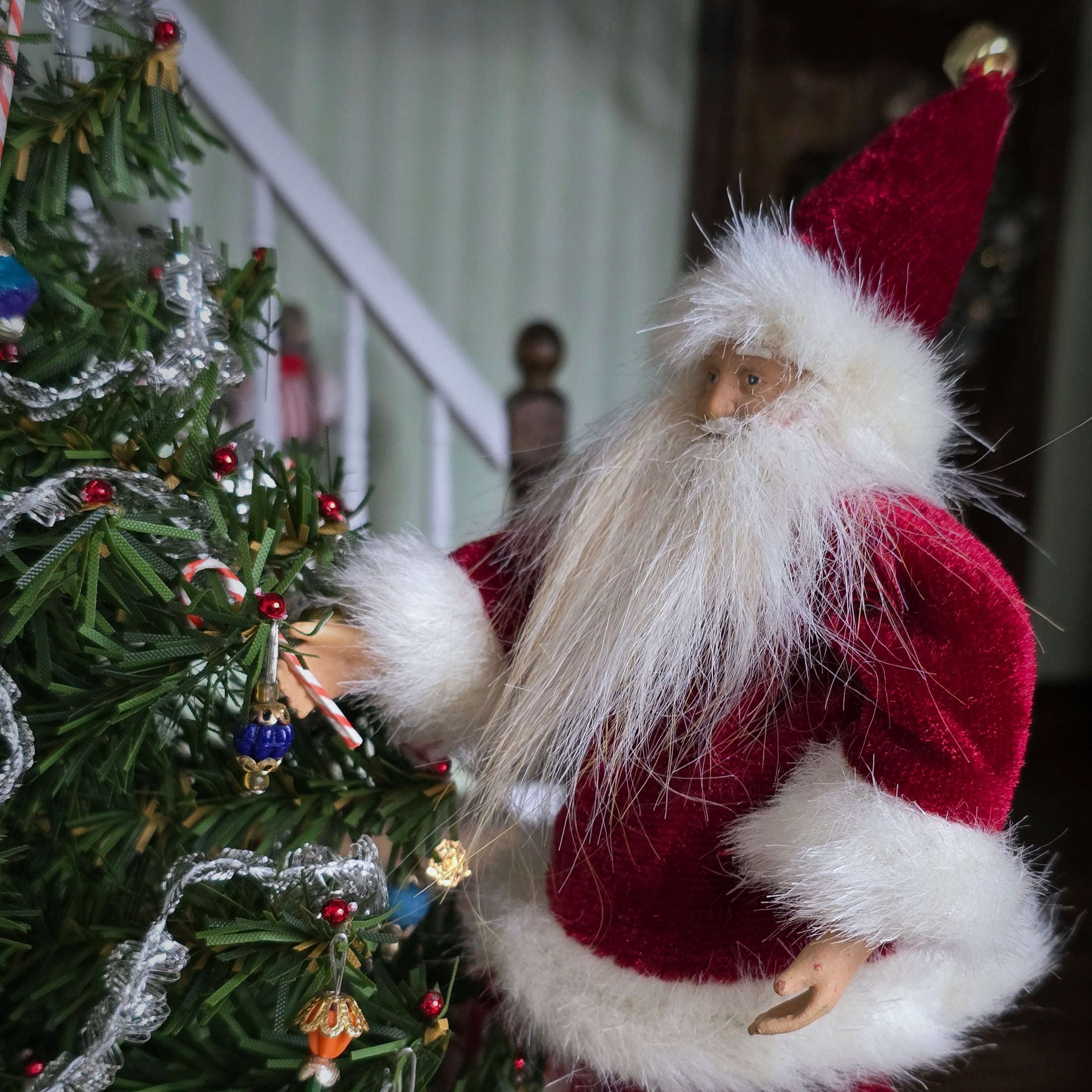 Santa Claus dollhouse doll next to a decorated Christmas tree indoors.
