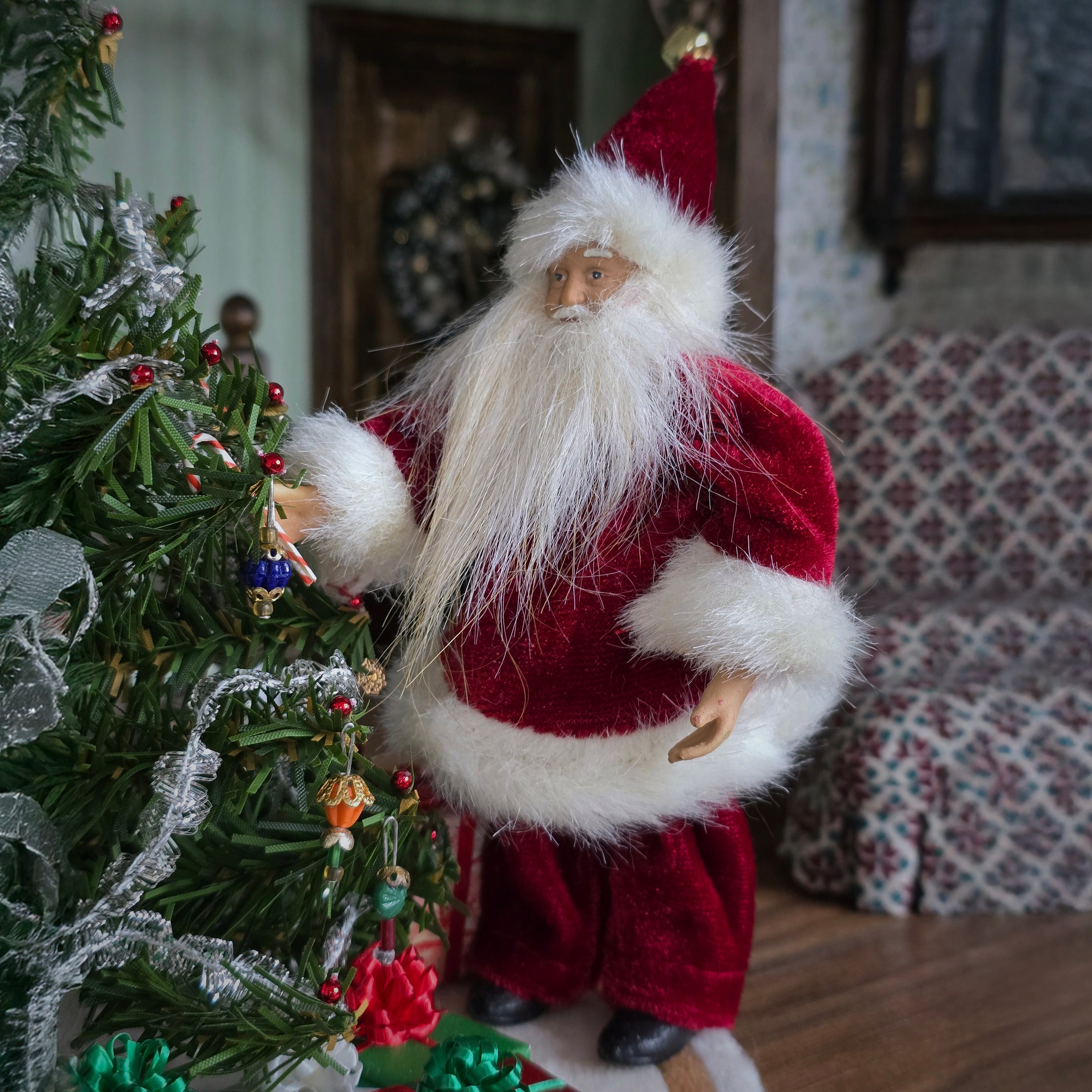 Santa Claus dollhouse doll decorating a Christmas tree in a cozy room.