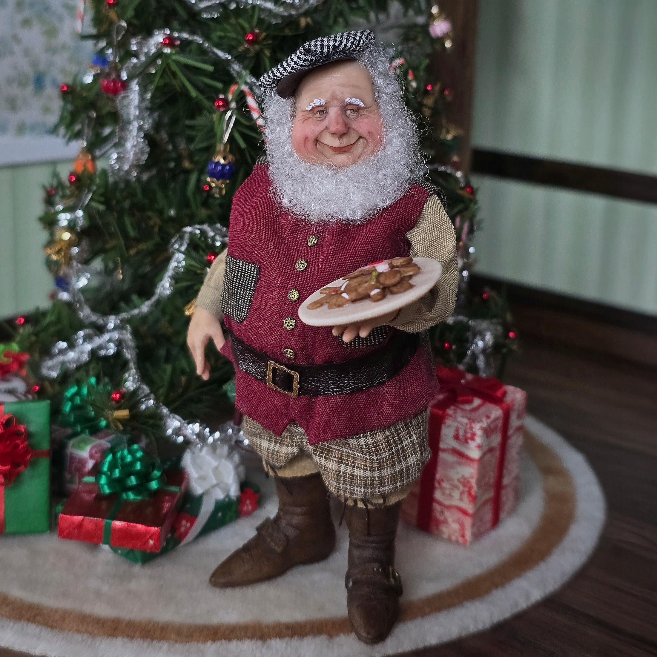 Old Christmas Elf doll with a beard holding cookies in front of a decorated Christmas tree.