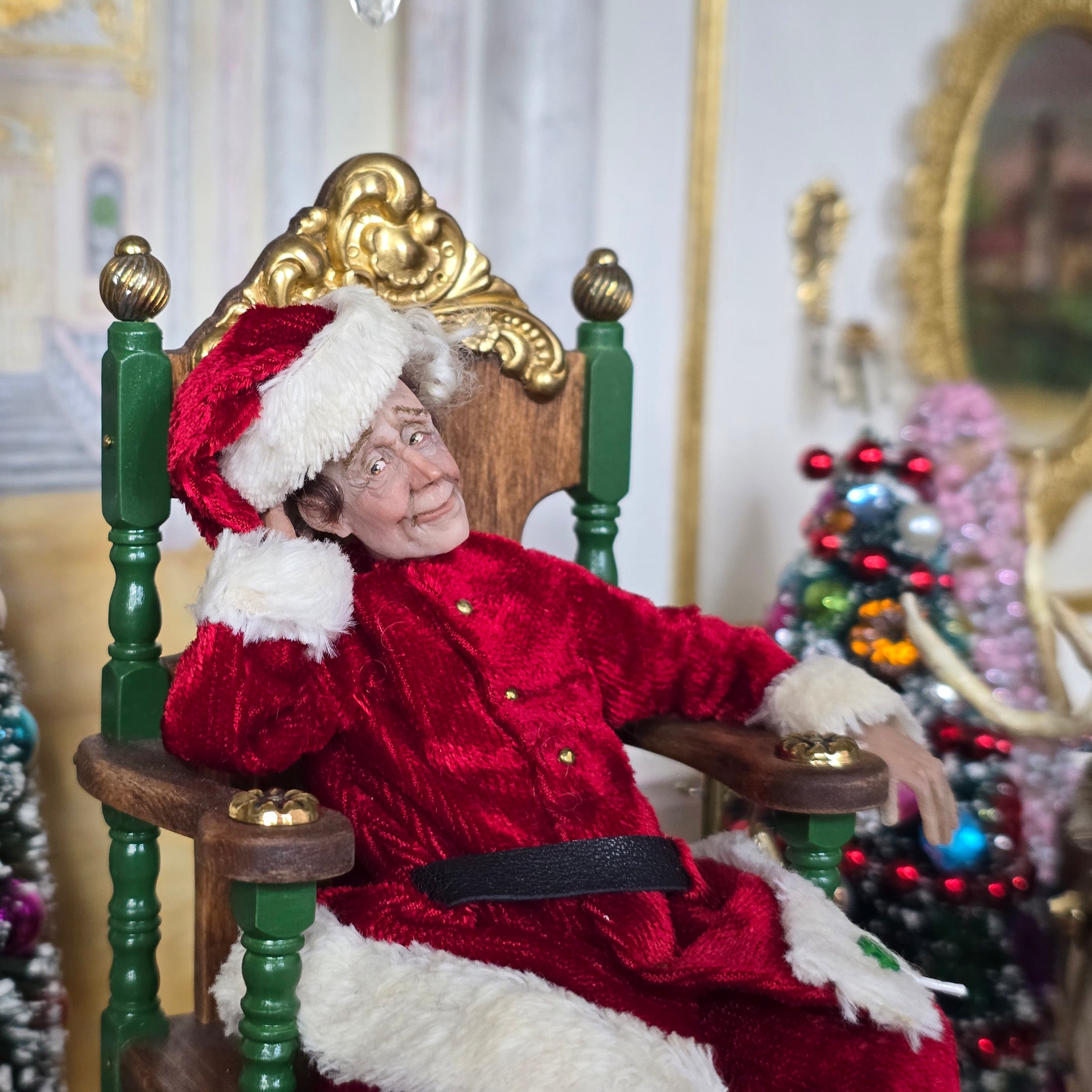 Santa dollhouse doll in a red costume sitting in a chair with Christmas decorations in the background