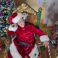 Load image into Gallery viewer, Santa dollhouse doll in a red outfit with white fur trim, sitting on an ornate chair in a festive setting.
