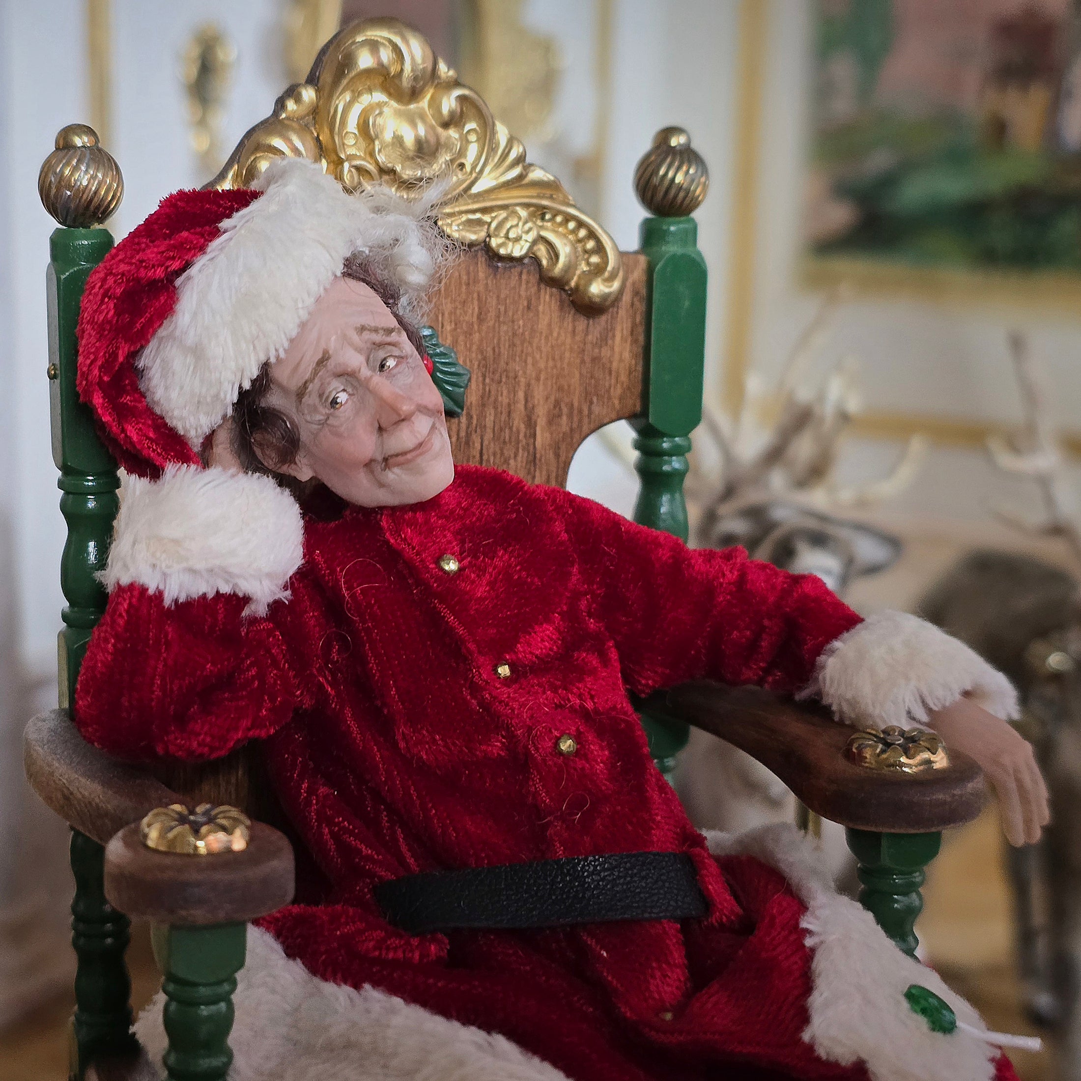 Santa dollhouse doll in a red outfit sitting on an ornate chair.
