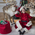 Load image into Gallery viewer, Santa dollhouse doll in a red suit sitting between two reindeer with a Christmas tree in the background.
