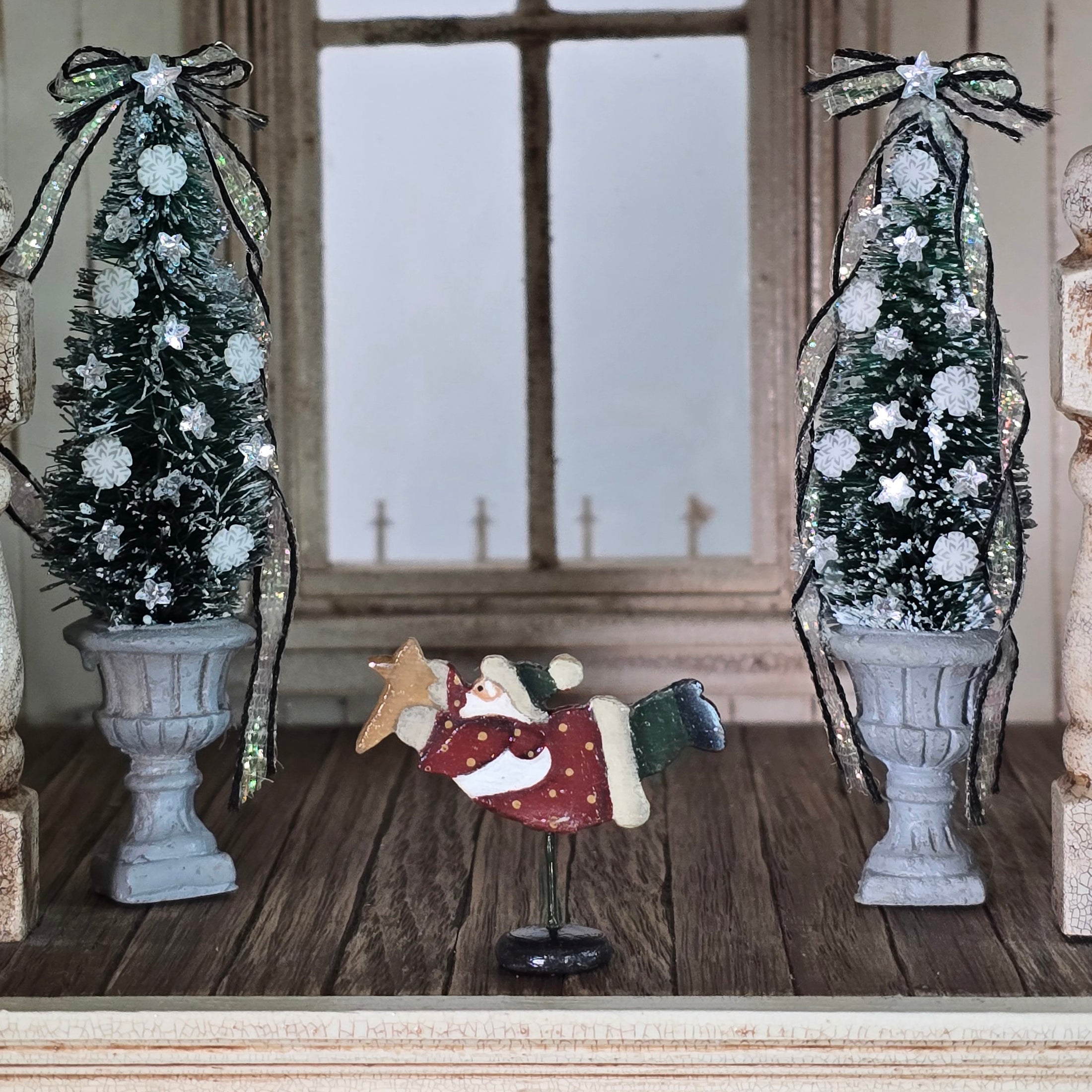 Decorative Christmas scene with two small trees, a flying Santa figure, and a star on a wooden floor.