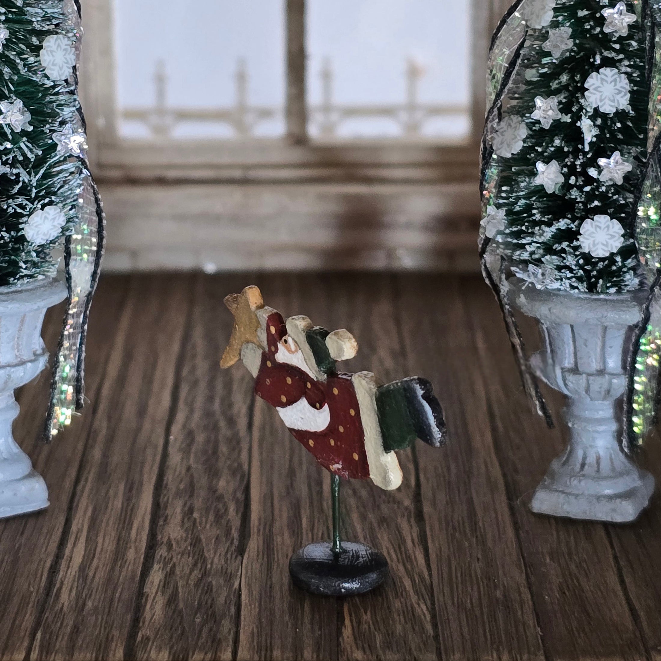 Small decorative figure of a  flying santa on a wooden surface with Christmas trees in the background.