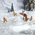Load image into Gallery viewer, Deer figurines in a snowy landscape with trees and a pond.
