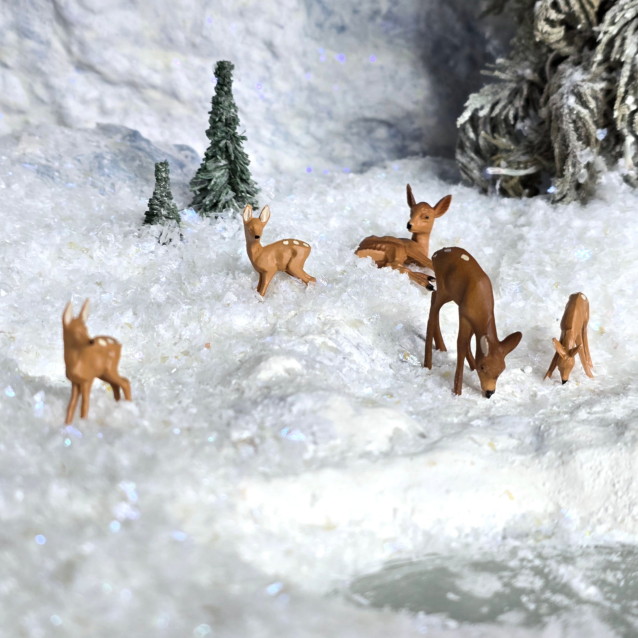 Deer figurines in a snowy landscape with trees and a pond.