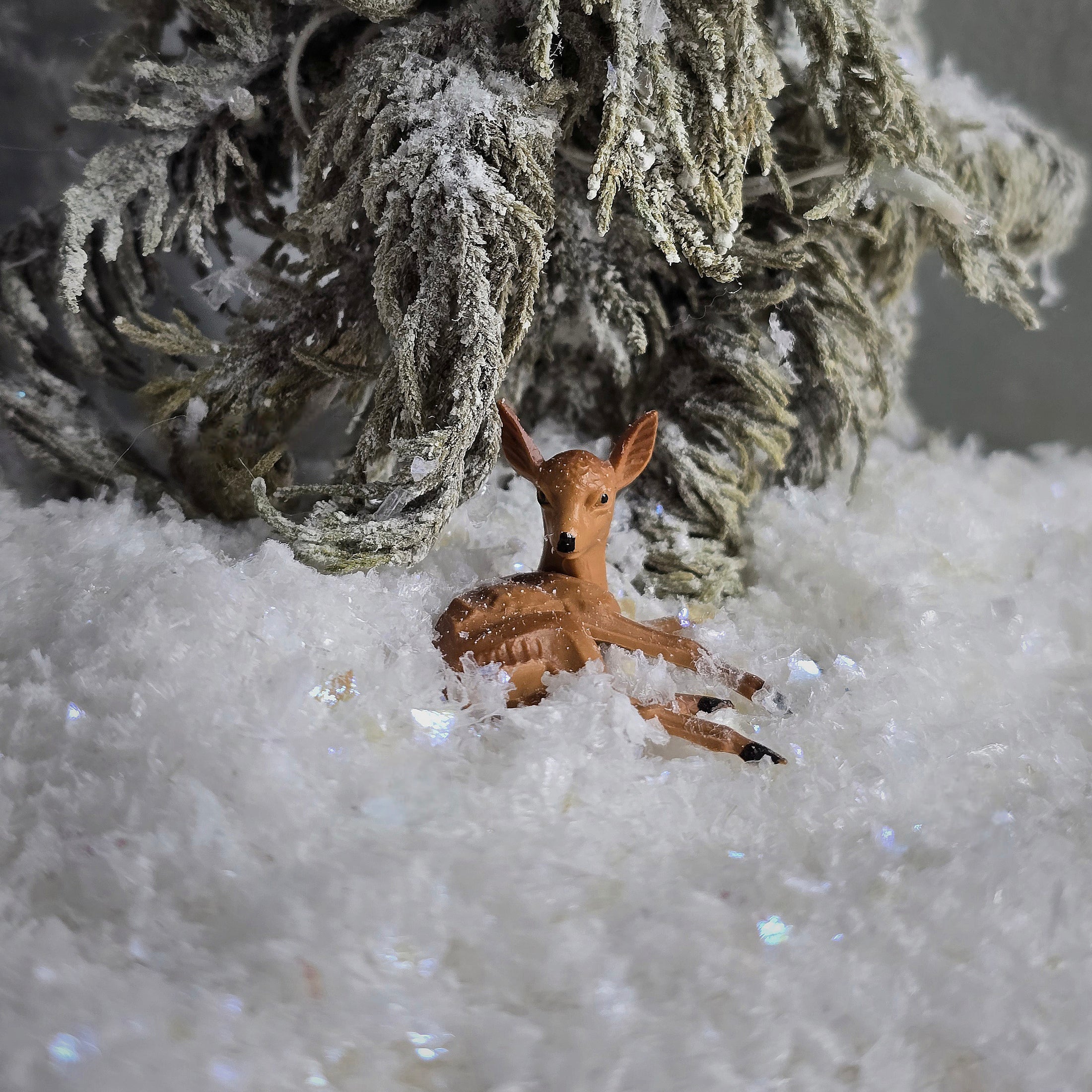 Small deer figurine in a snowy landscape with a textured branch above