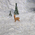Load image into Gallery viewer, Small deer figurine standing on a snowy surface with two small trees in the background.
