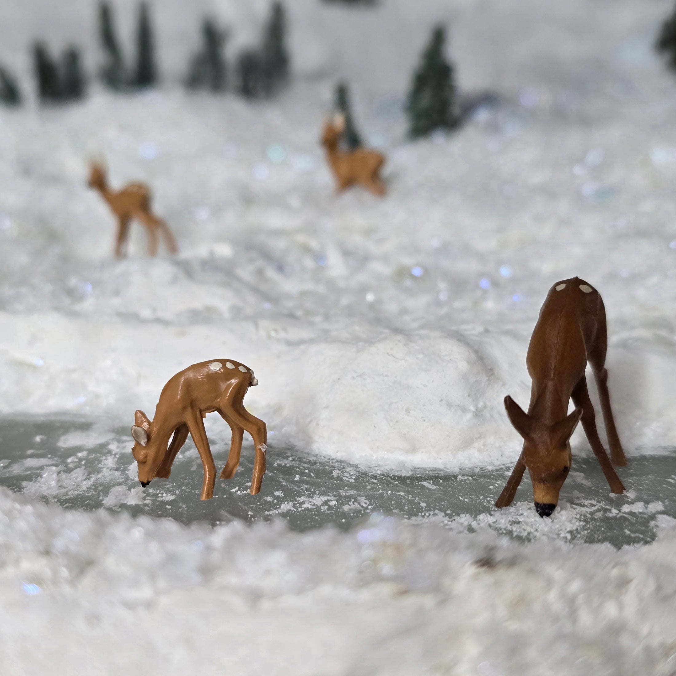 Model deer figures on a snowy surface with a blurred forest background