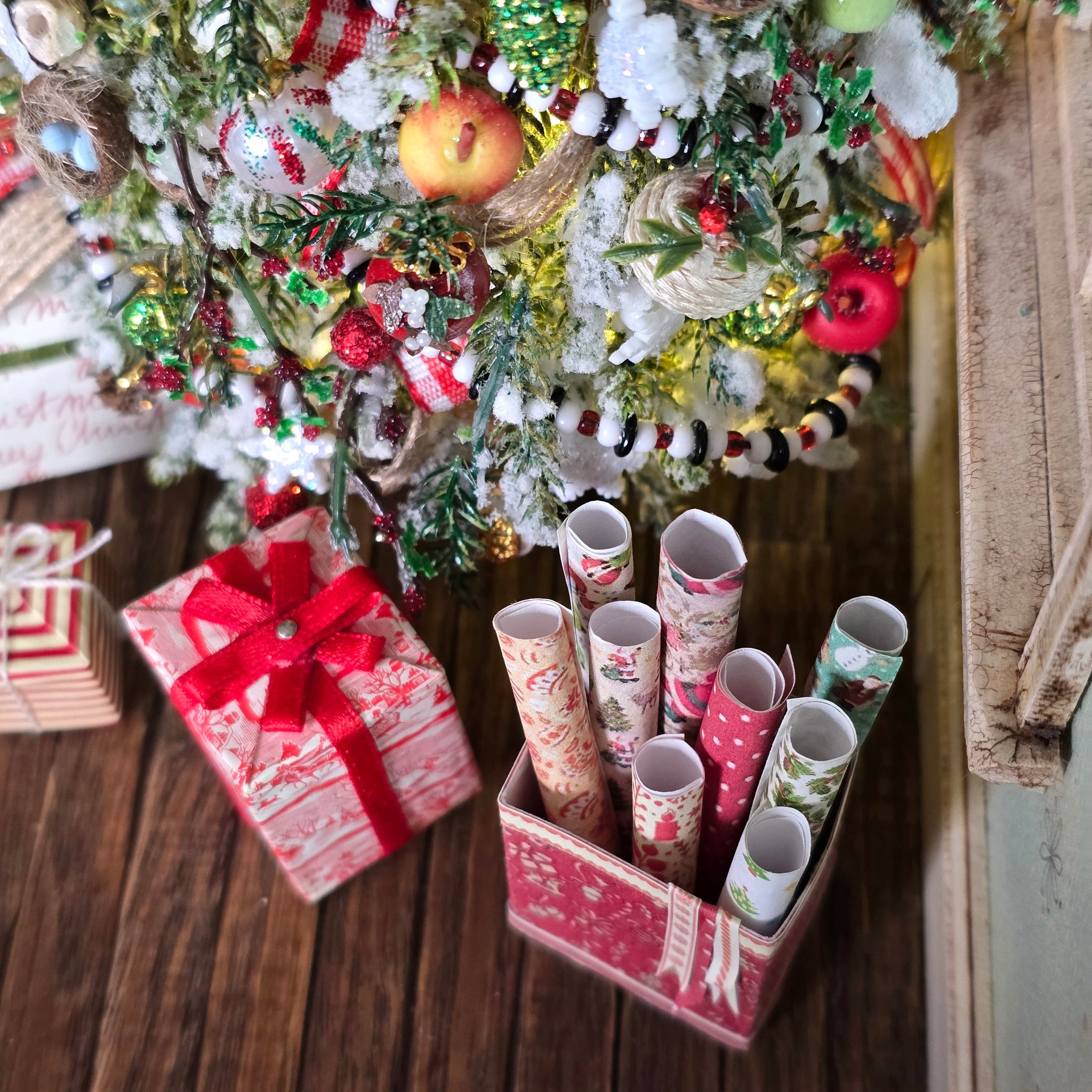 Decorative Christmas scene with a tree, presents, and paper rolls on a wooden floor.
