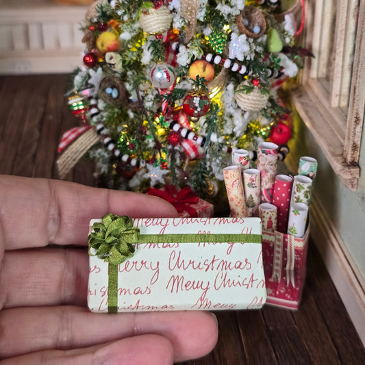 Hand holding a miniature Christmas gift with a tree in the background