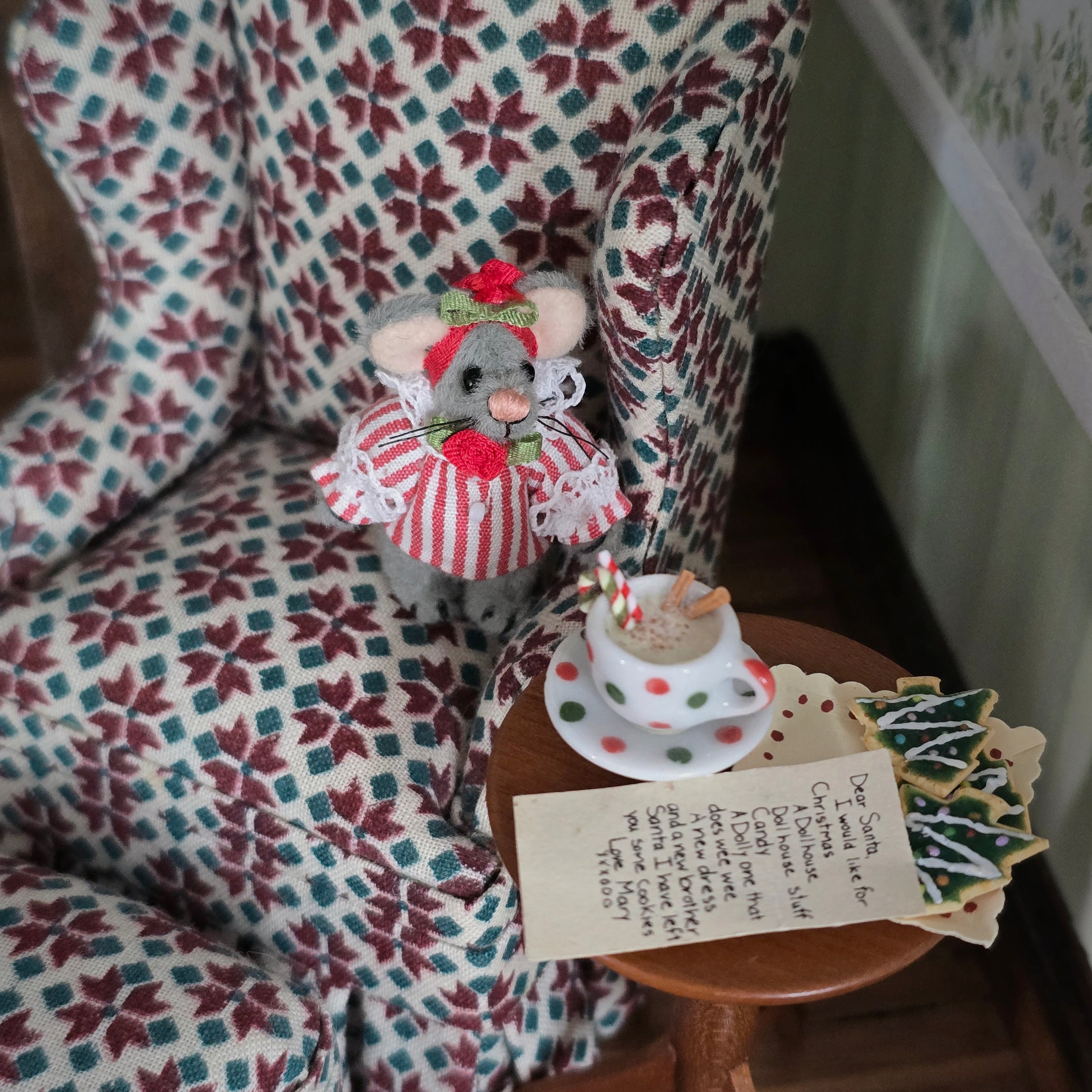 Small toy mouse in a festive outfit sitting on a chair with a miniature table and tea set.