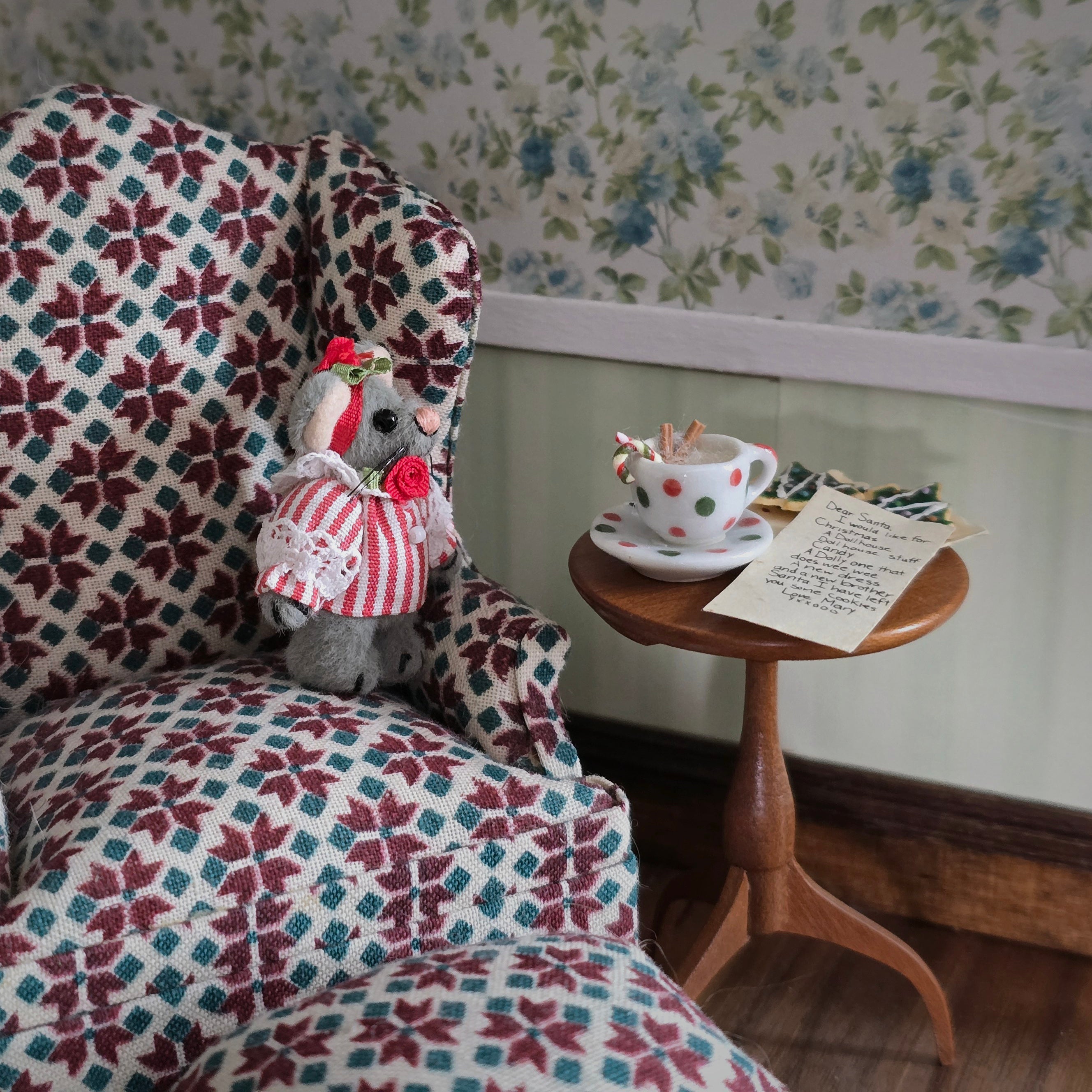 Small stuffed mouse in a patterned chair with a side table featuring a teacup and saucer.