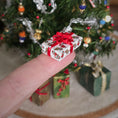 Load image into Gallery viewer, Miniature Christmas gift box with red ribbon held in front of a decorated Christmas tree.
