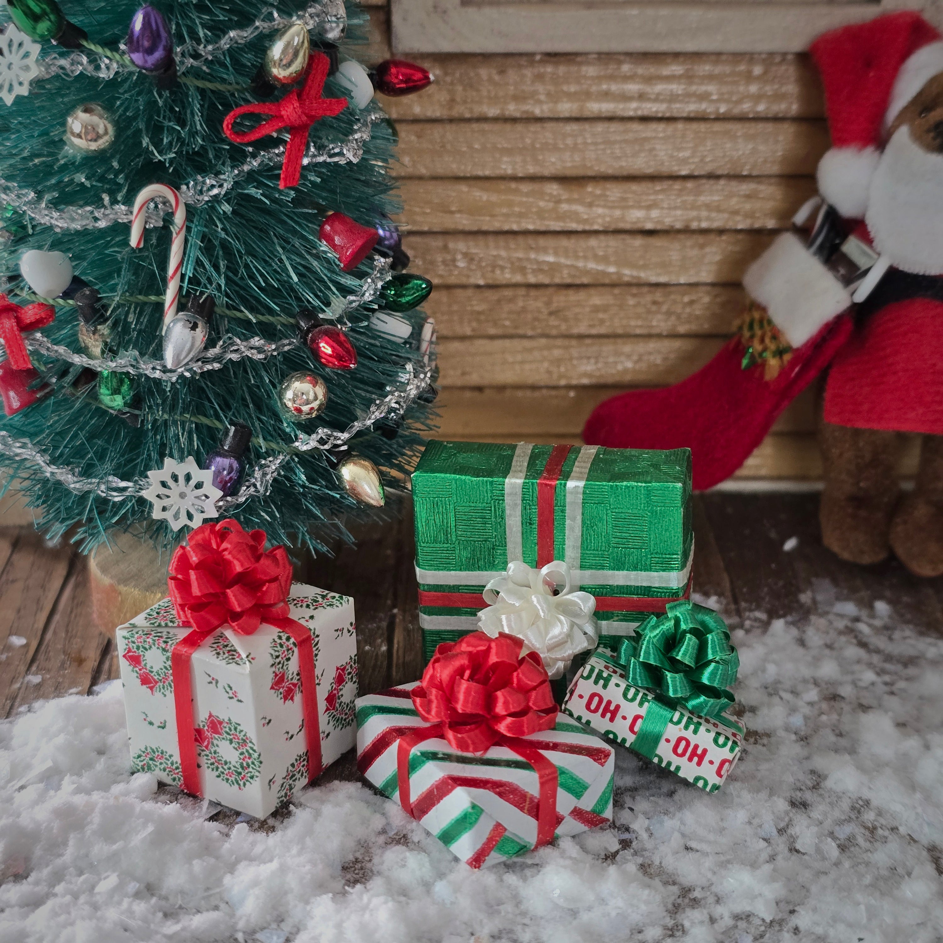 Christmas scene with a small tree, presents, and a Santa Claus figure on a snowy ground.