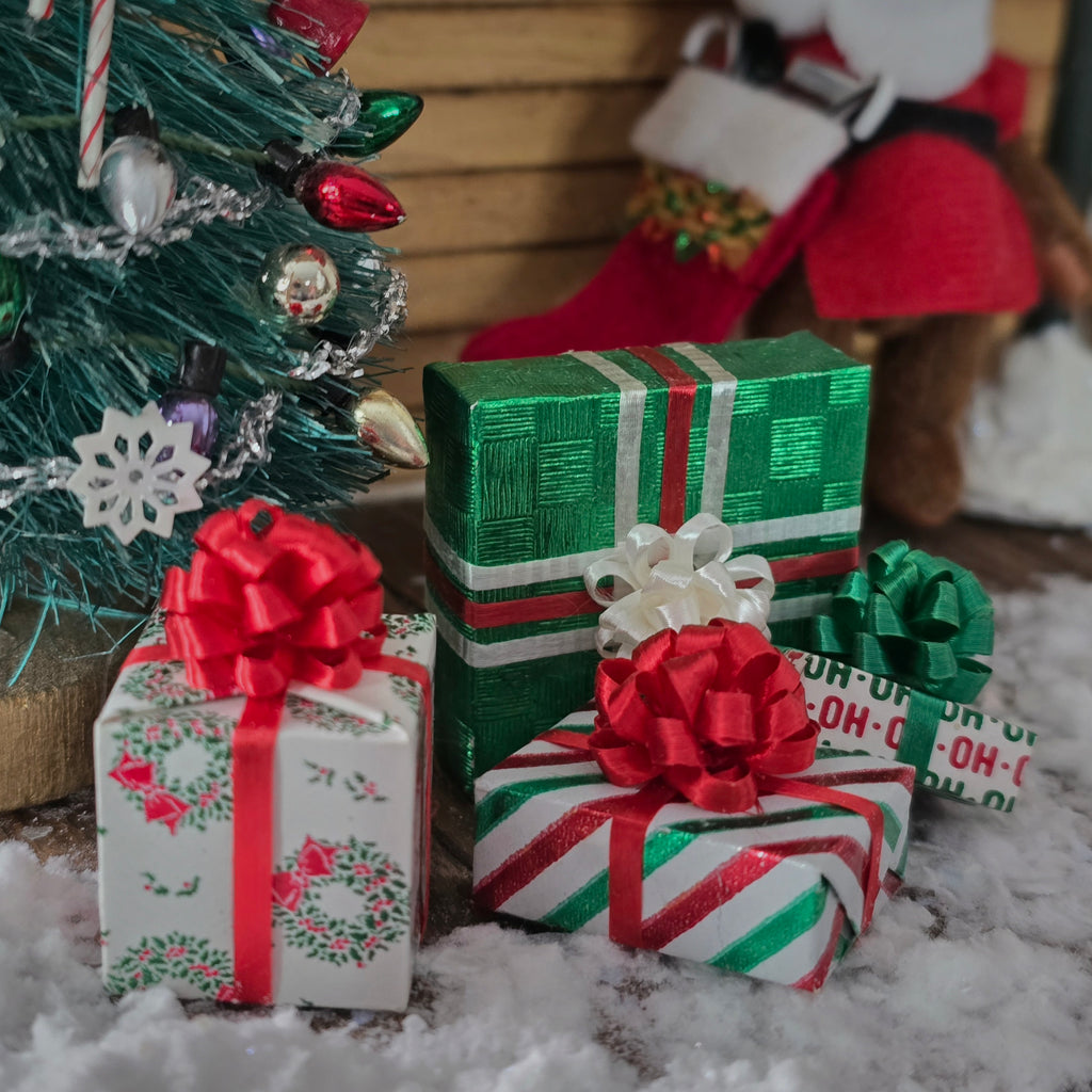 Decorative Christmas presents with red and green ribbons in front of a small Christmas tree.