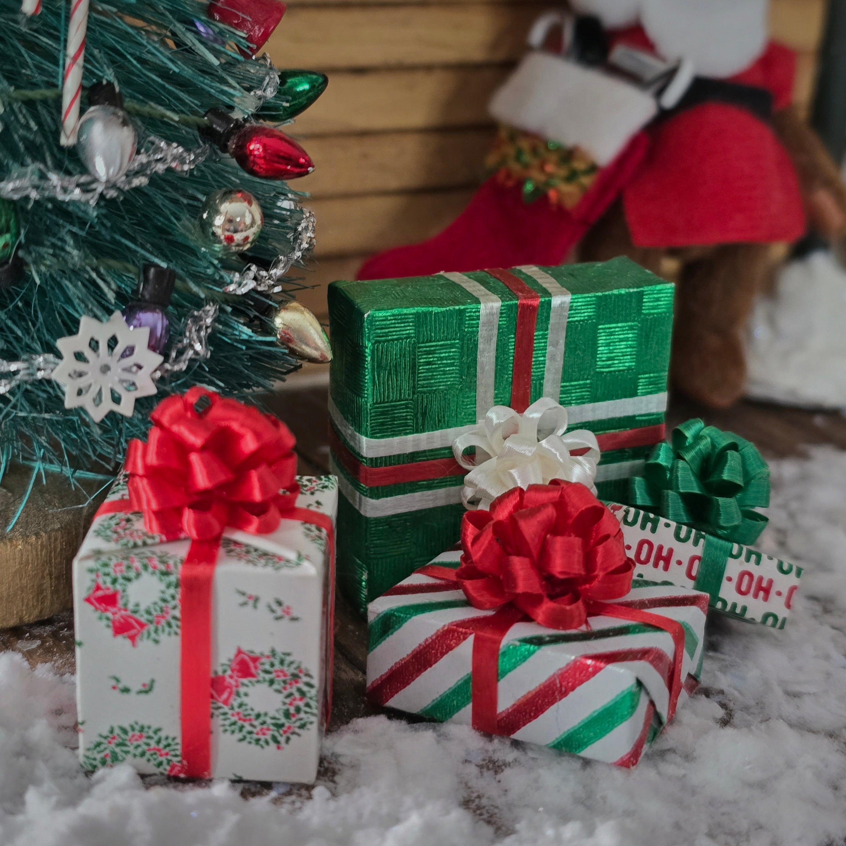 Decorative Christmas presents with red and green ribbons in front of a small Christmas tree.