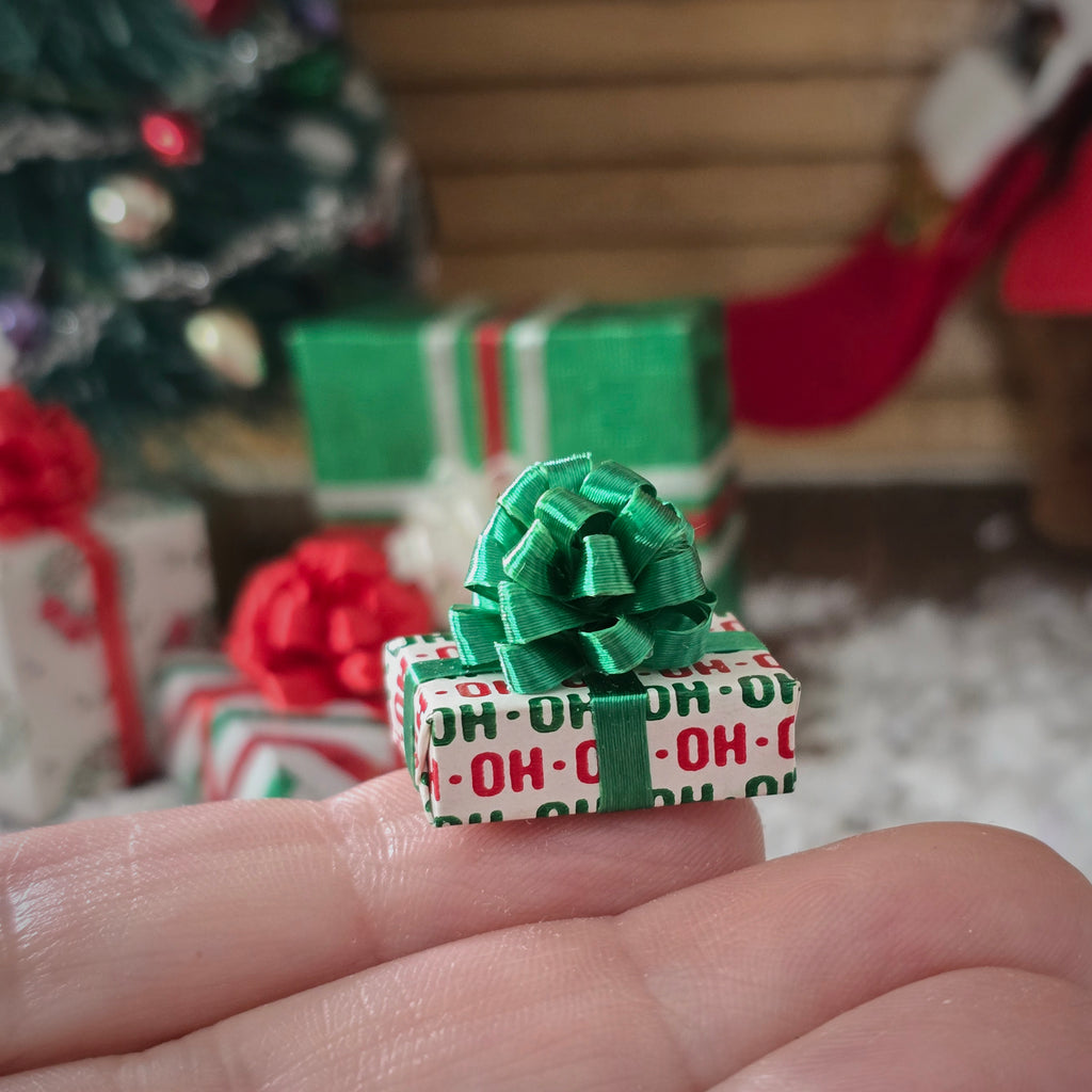 Small gift box with a green ribbon held in a hand, with Christmas decorations in the background.