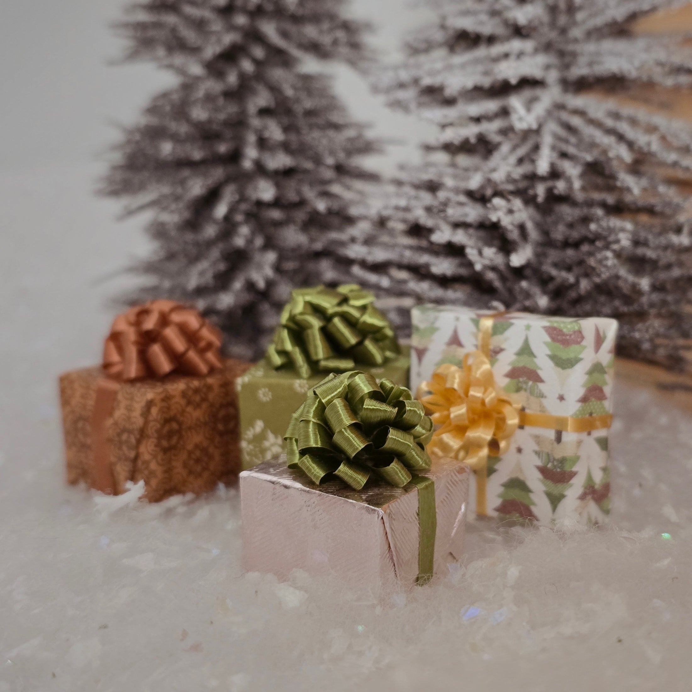 Three gift boxes with decorative bows in front of a snow-covered tree.