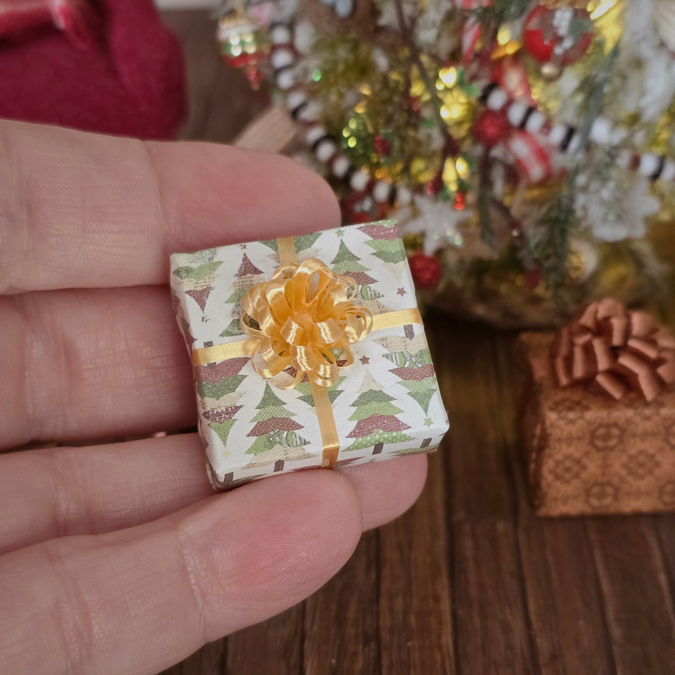 Miniature gift box with a gold bow held in a hand, with a festive background.