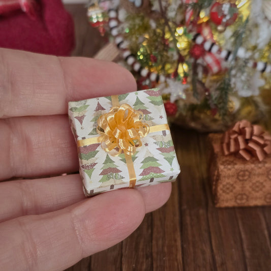Miniature gift box with a gold bow held in a hand, with a festive background.
