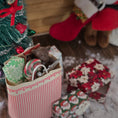 Load image into Gallery viewer, Small Christmas tree with decorative items and a striped bag on a wooden floor.
