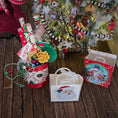 Load image into Gallery viewer, Decorative Christmas scene with gift bags, a small tree, and festive items on a wooden surface.
