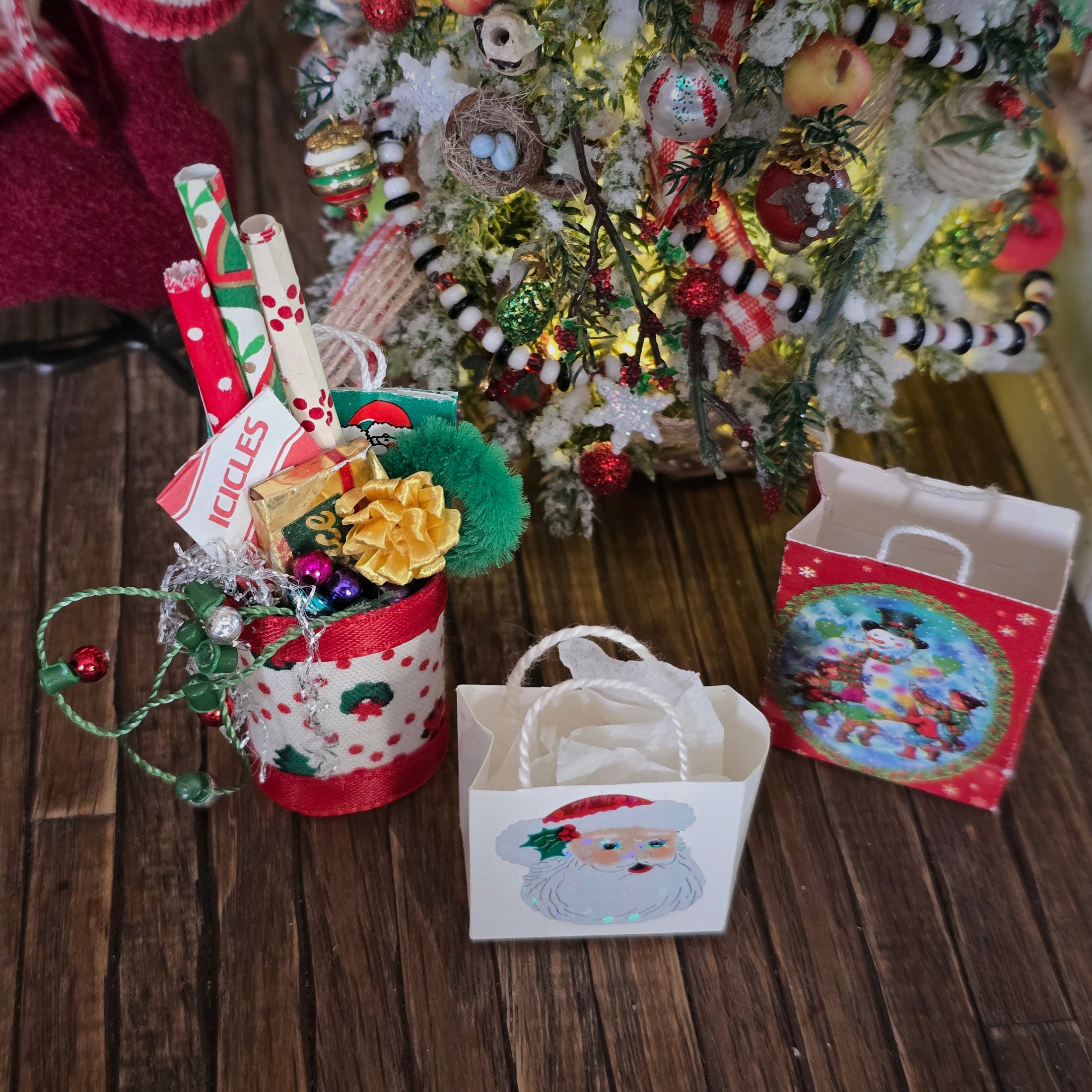 Decorative Christmas scene with gift bags, a small tree, and festive items on a wooden surface.