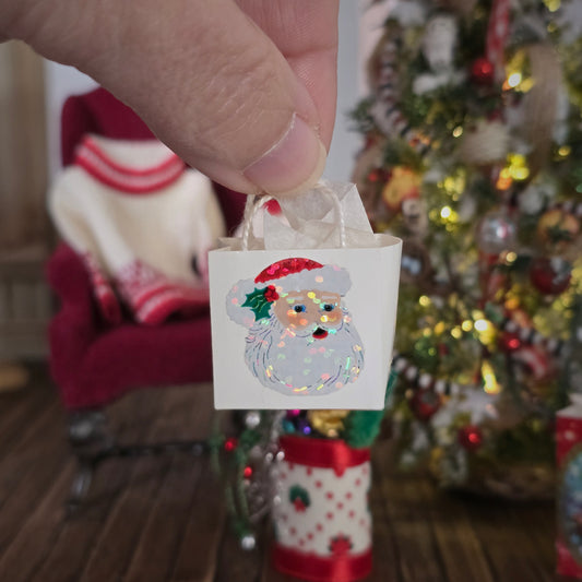 Small decorative bag with a Santa Claus design held by a hand in front of a Christmas tree.