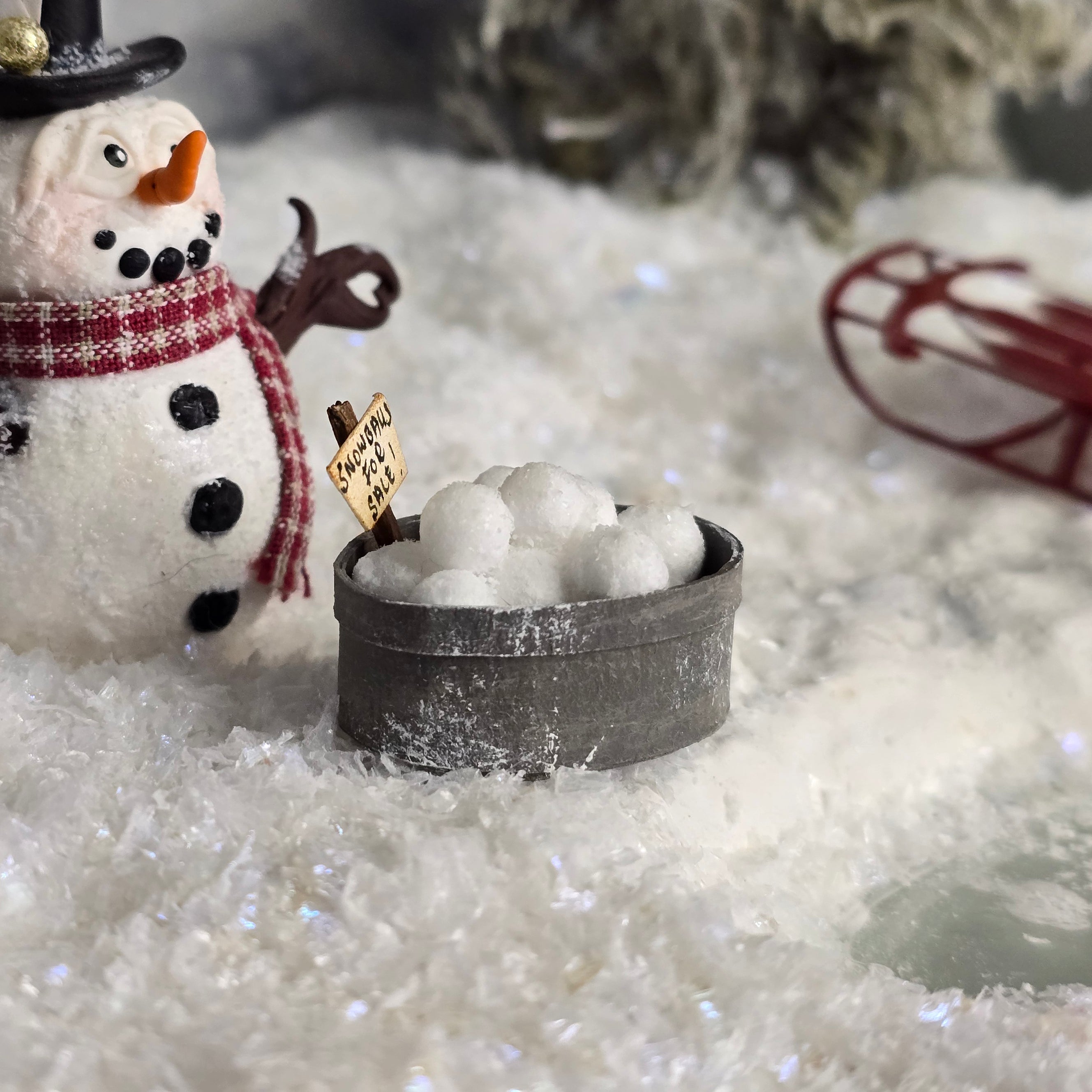 miniature snowman figurine with a bucket of snowballs on a snowy surface.