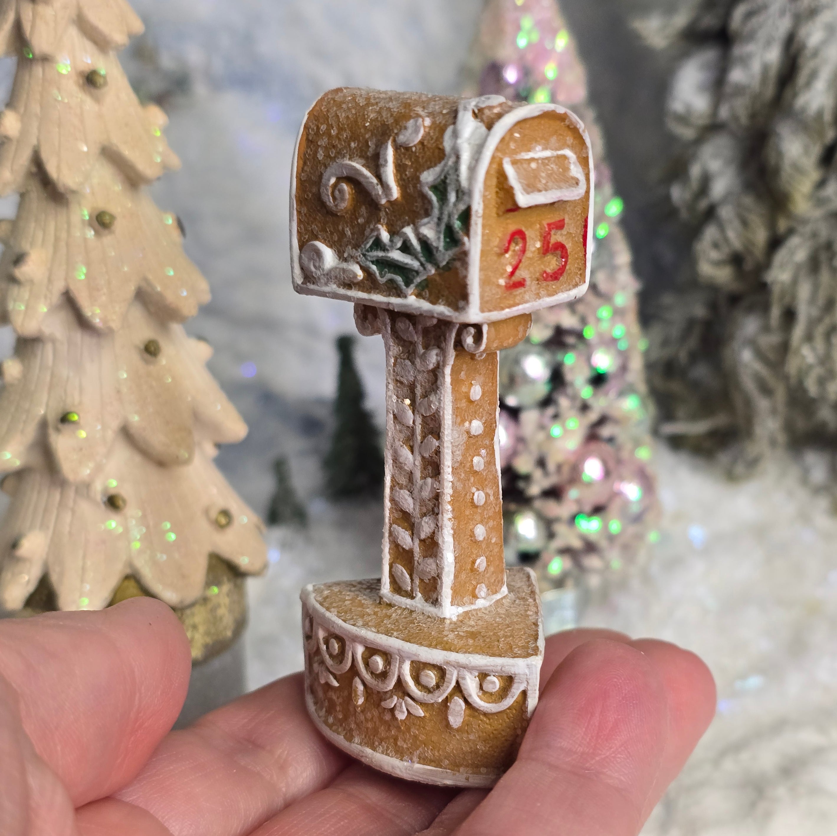 Decorative gingerbread miniature mailbox held in a hand with Christmas trees in the background