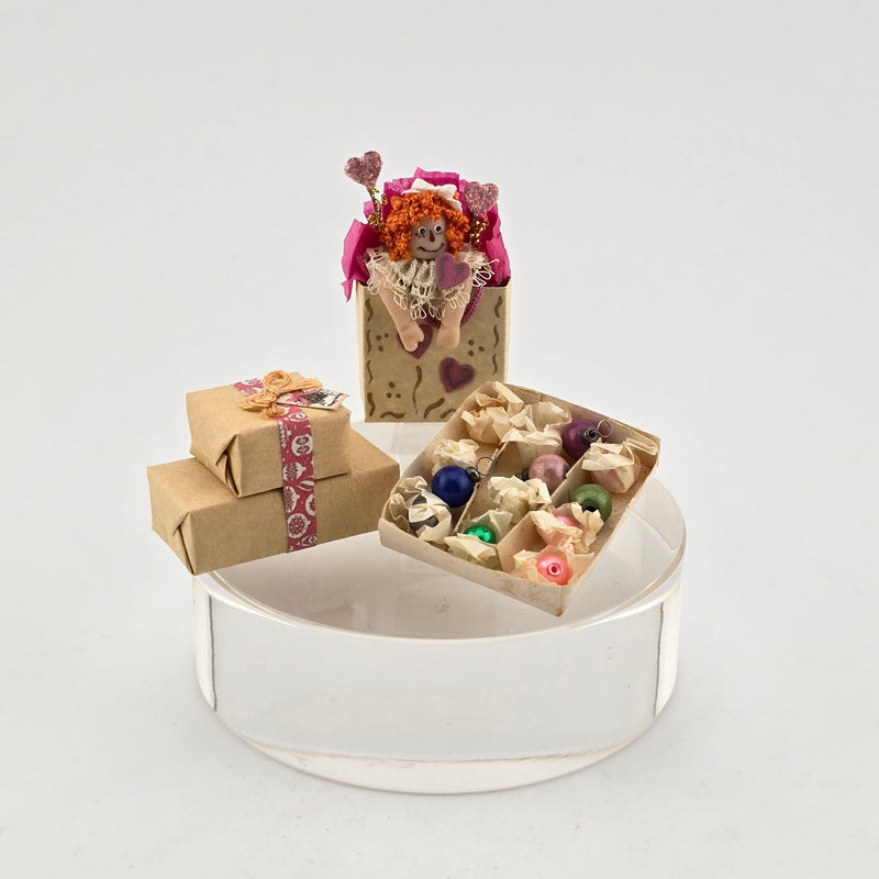 Dollhouse miniatures including a small doll, wrapped gift, and decorative boxes