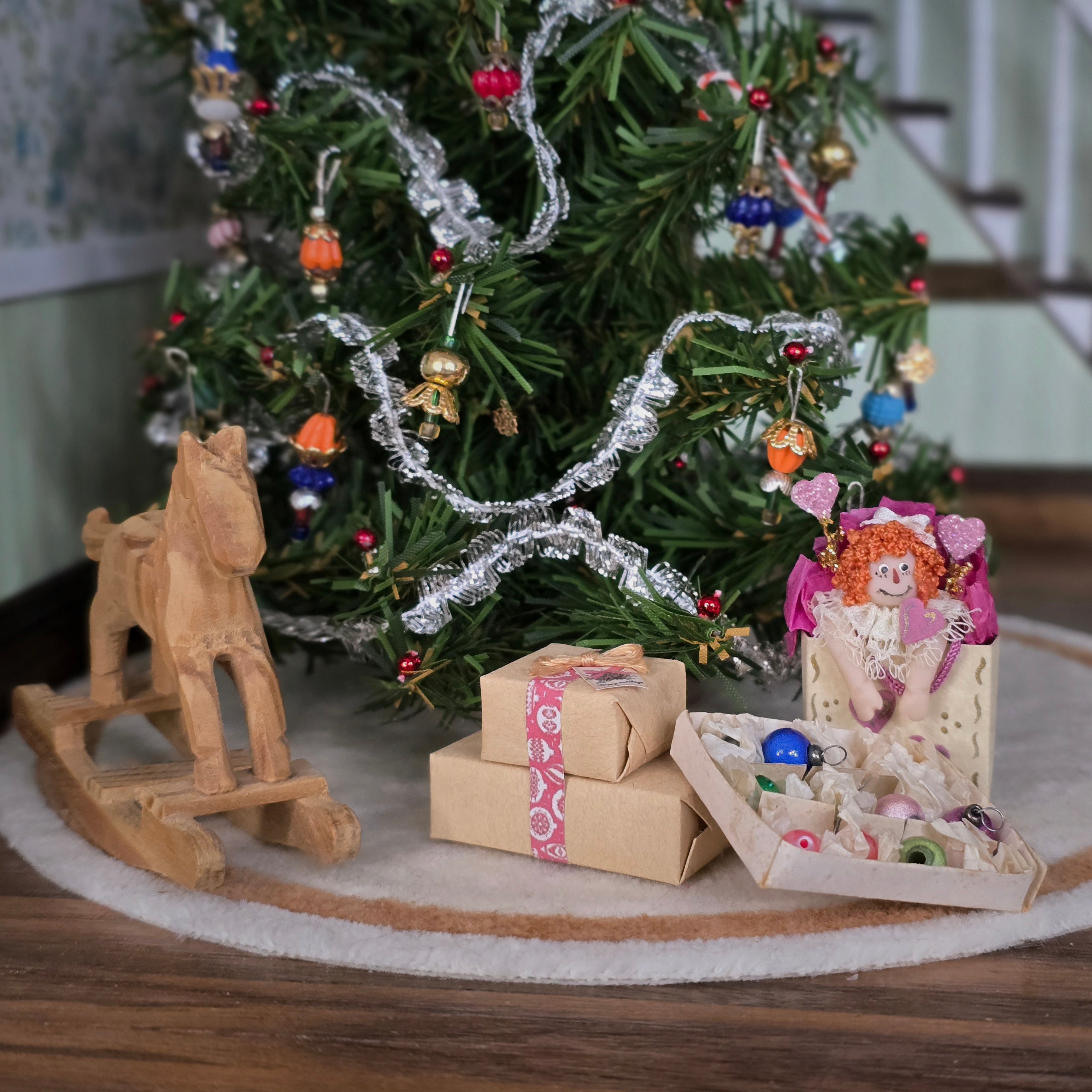 Dollhouse miniatures with wrapped gifts, and a doll in front of a Christmas tree.