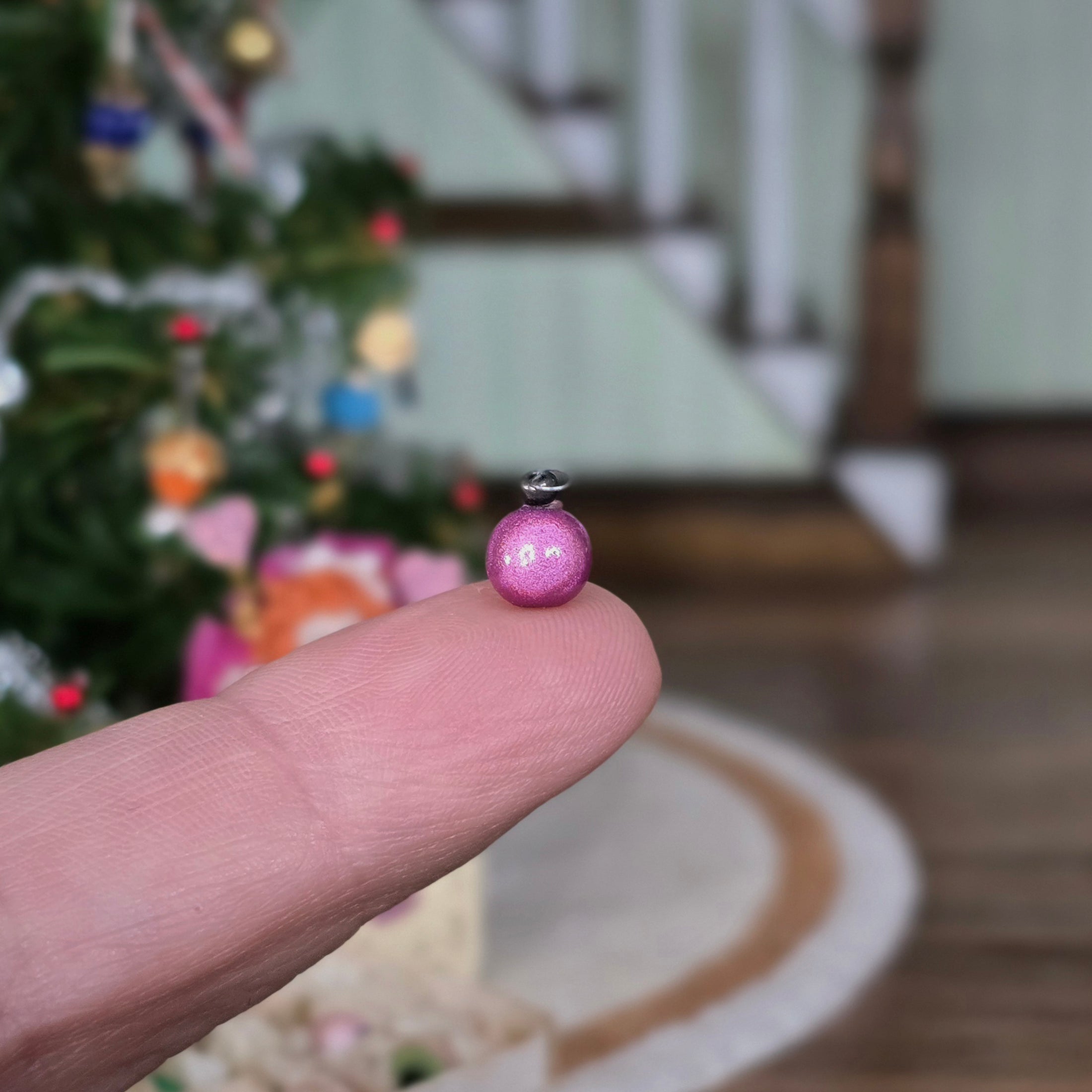 Pink ornament held on a finger with a blurred Christmas tree in the background