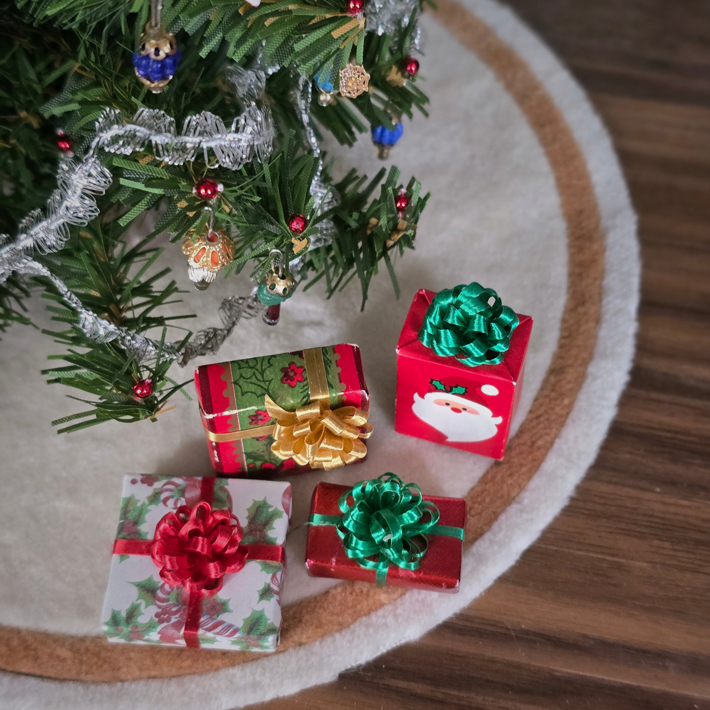 Miniature Christmas presents with decorative ribbons near a small decorated tree on a wooden surface.