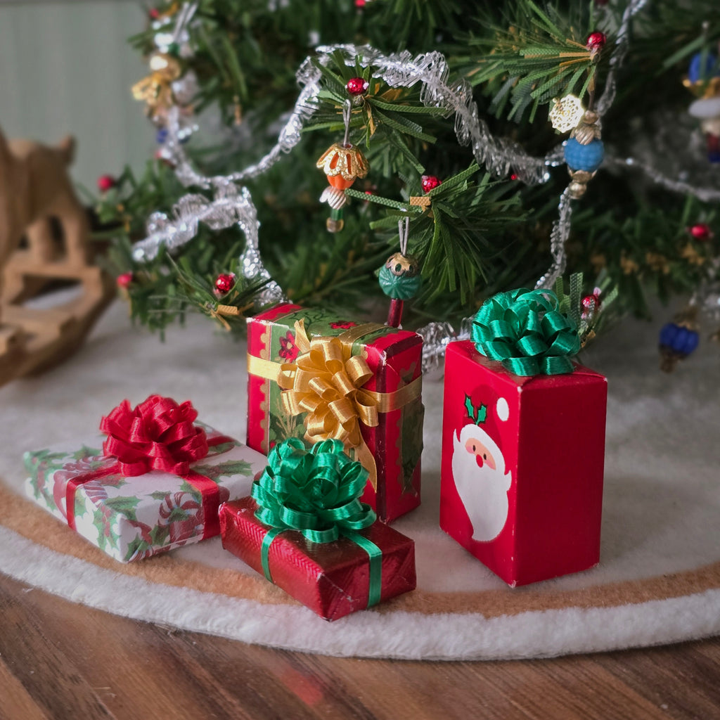Small Christmas gift boxes with ribbons and Santa Claus design in front of a decorated tree.