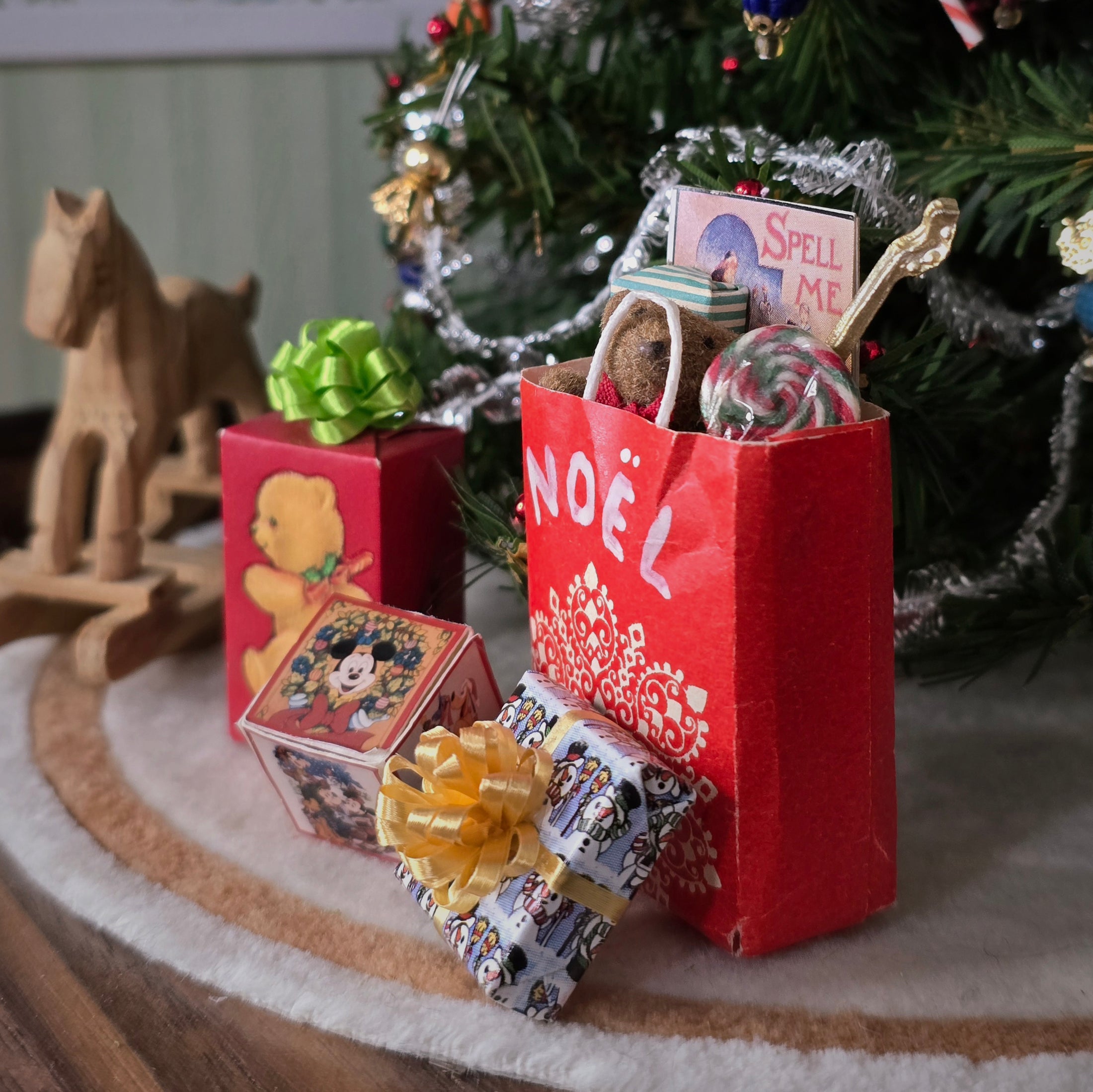 Miniature Christmas scene with gift boxes and a 'NOËL' bag in front of a decorated tree.