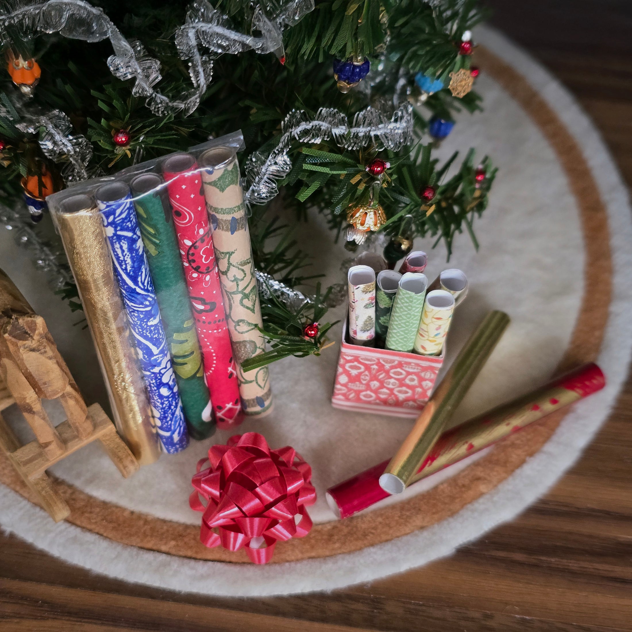 Decorative rolls of paper and bow on a round rug with a Christmas tree in the background.